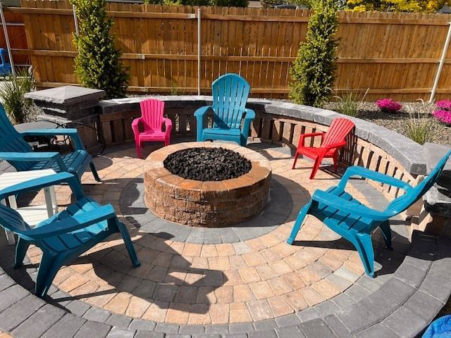 Outdoor fire pit surrounded by brightly colored Adirondack chairs on a patterned brick patio.