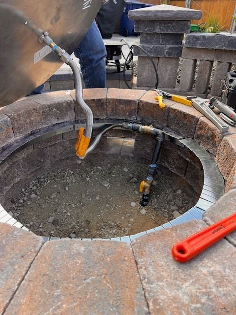 Person pouring water into a circular brick fire pit with gas line and tools.