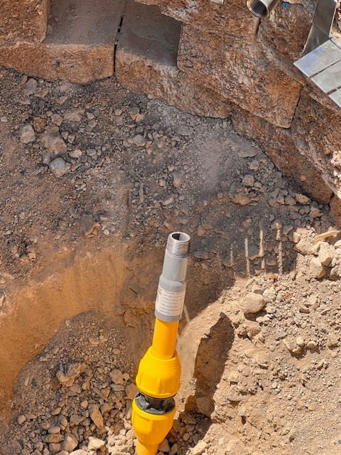 Yellow hose with metal fitting in dusty construction site, near stone blocks.
