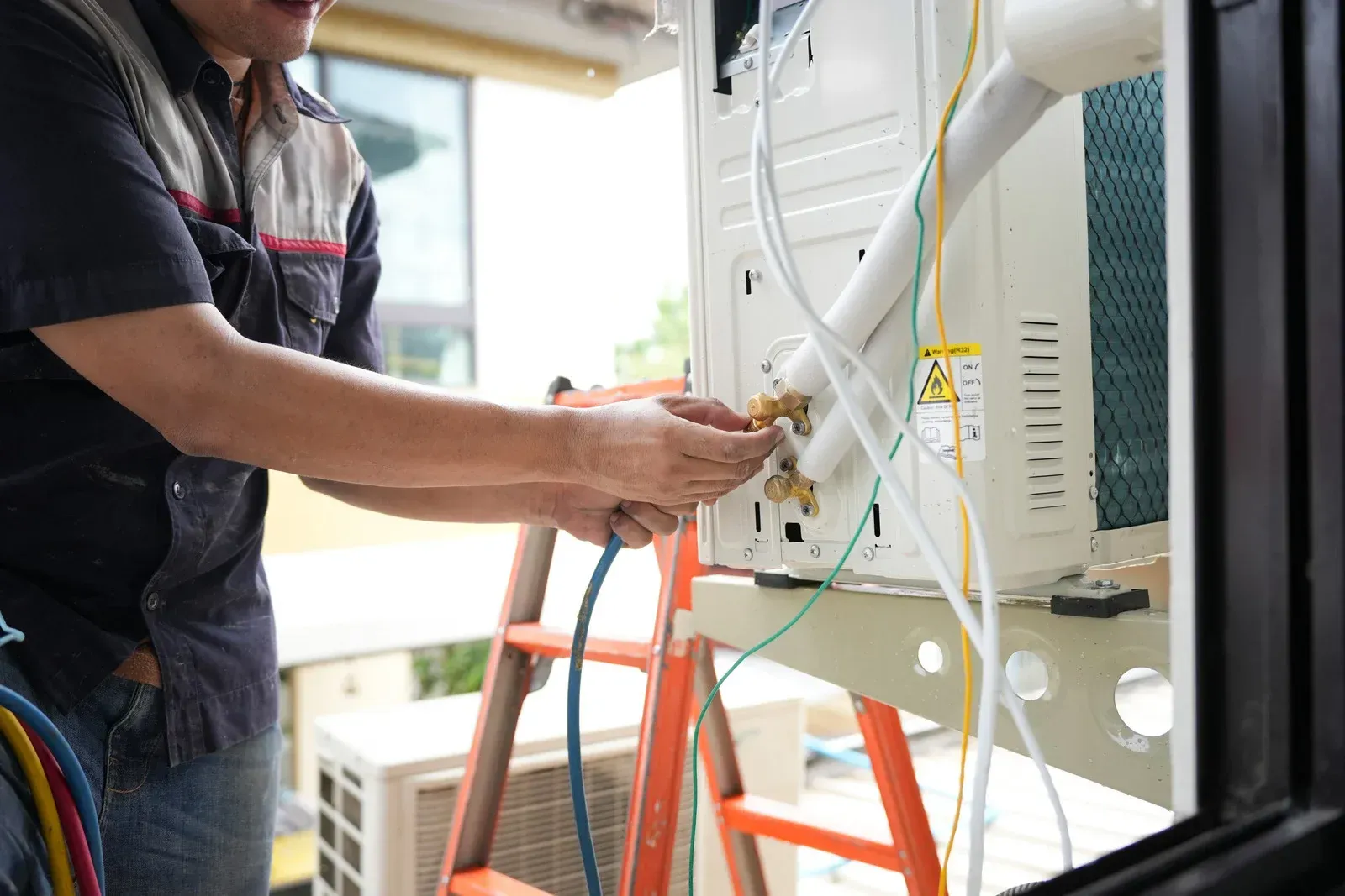 HVAC technician connecting wires to an outdoor air conditioning unit.
