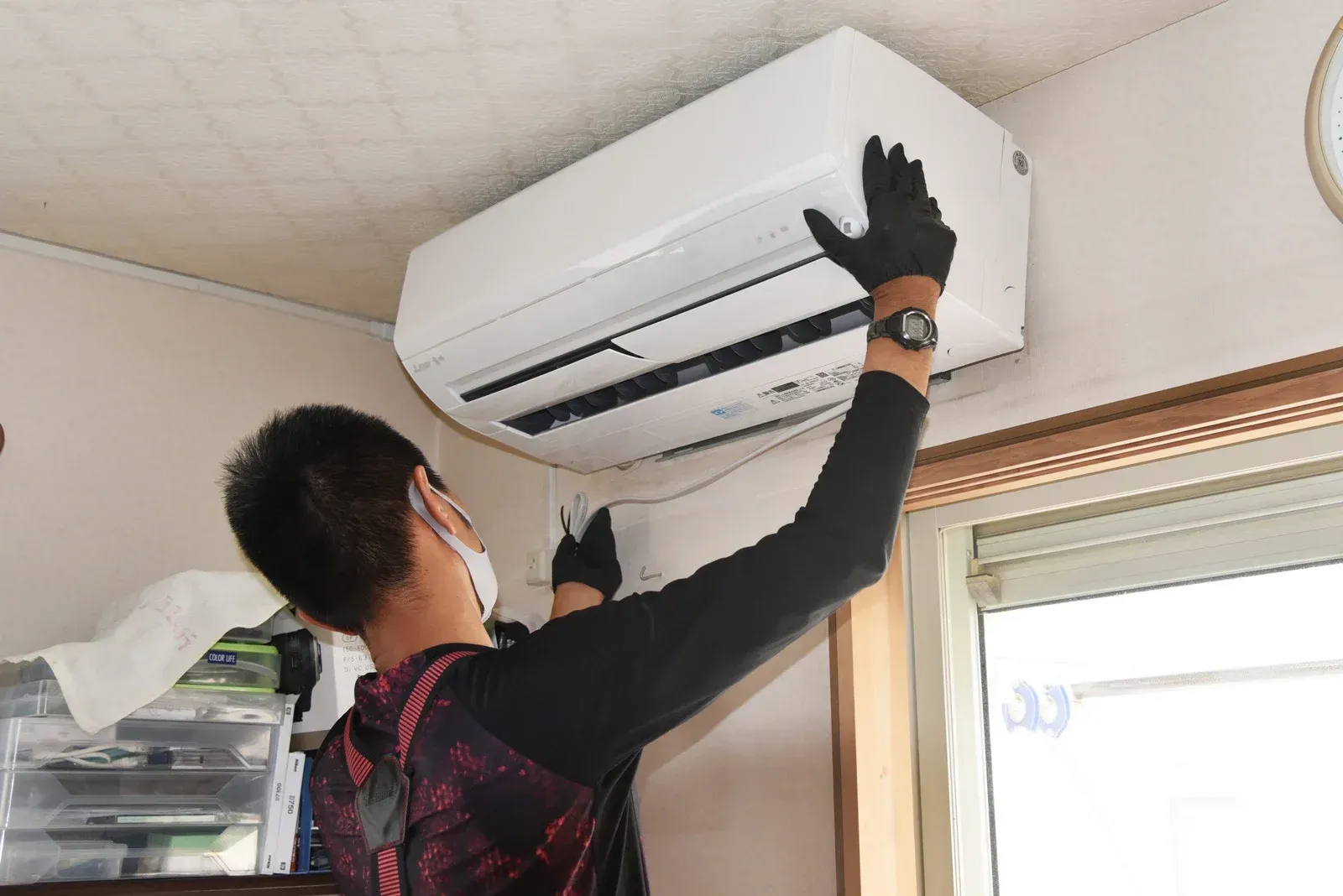 Person in gloves installing an air conditioner unit on a ceiling.