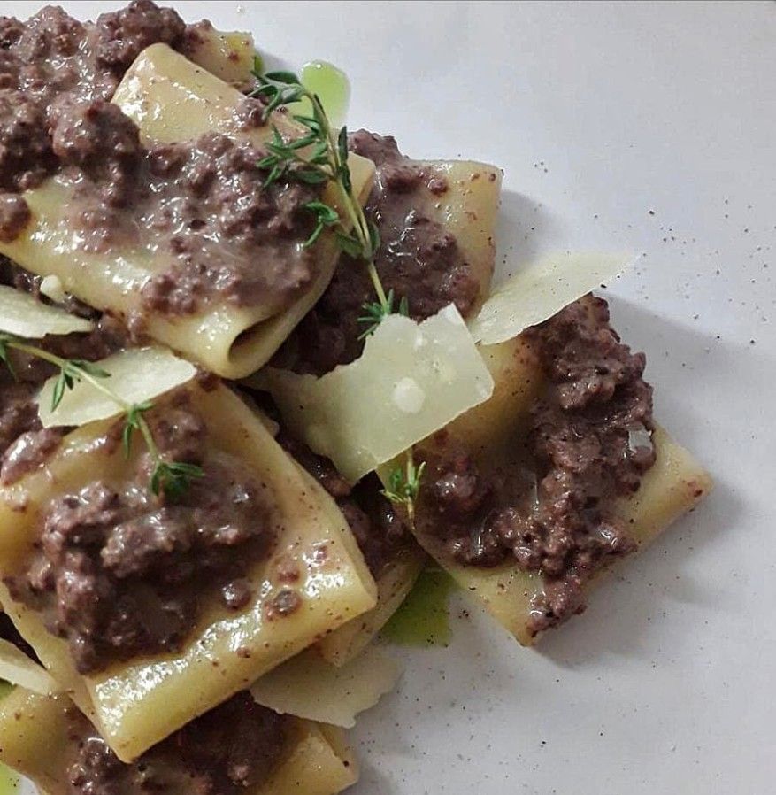 Pasta with meat sauce and shaved cheese on a white plate, garnished with herbs.