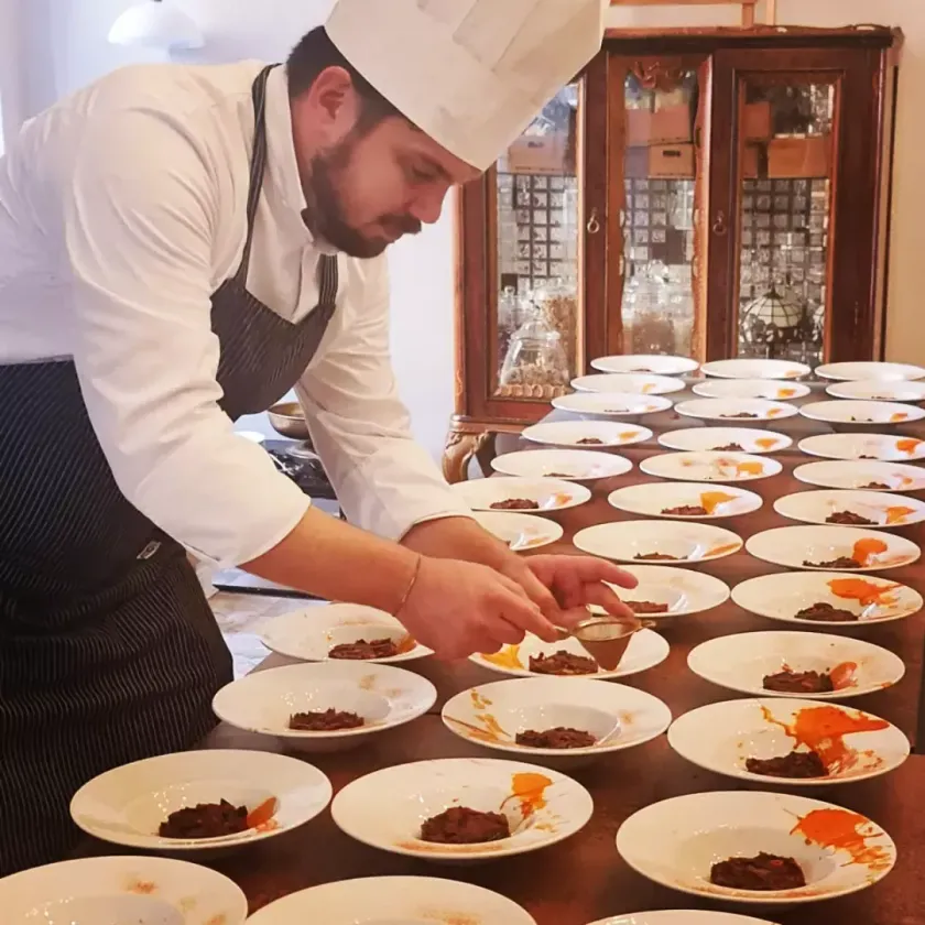 Chef plating dishes on white plates in a professional kitchen or dining room