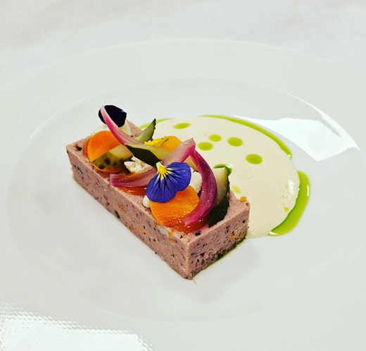 Gourmet dessert plate with chocolate cake, fruit garnish, and white mousse with green sauce dots