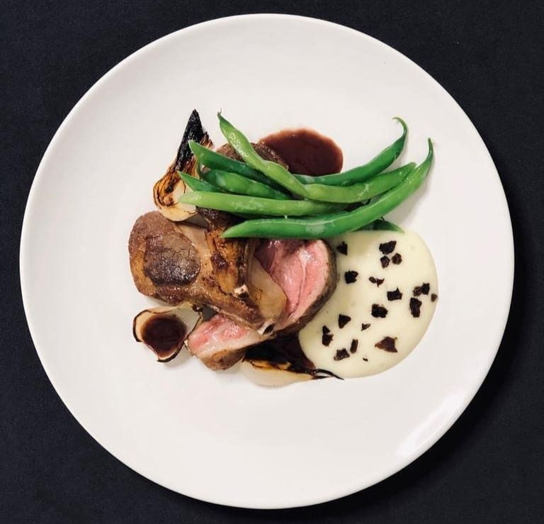 Plated gourmet steak with green beans and creamy sauce on a white plate