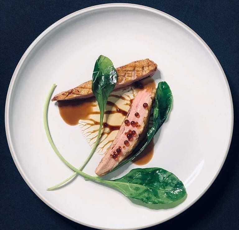 Plated gourmet fish with green leaves and brown sauce on a white dish