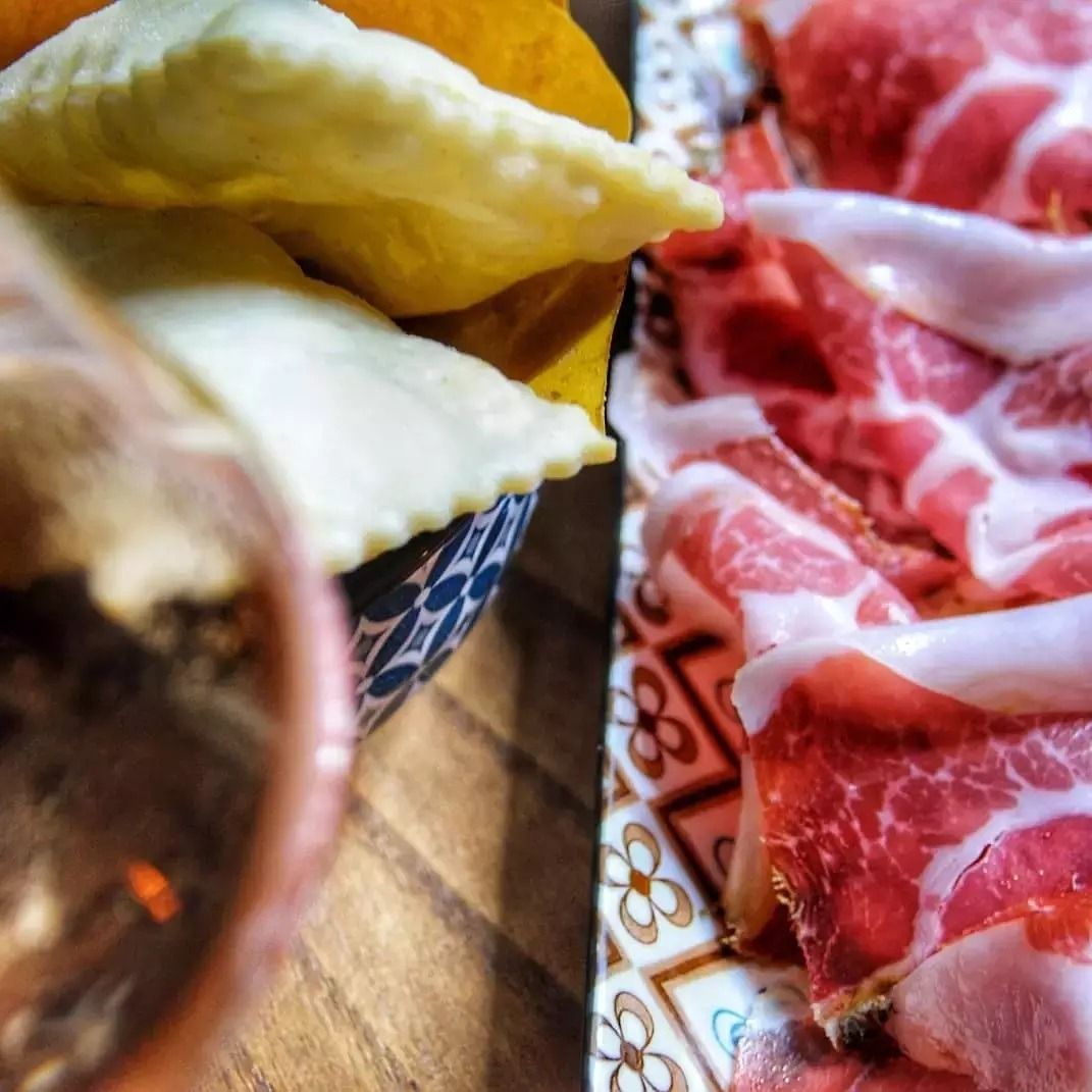 Dumplings on a table beside marbled slices of meat and a glass of wine