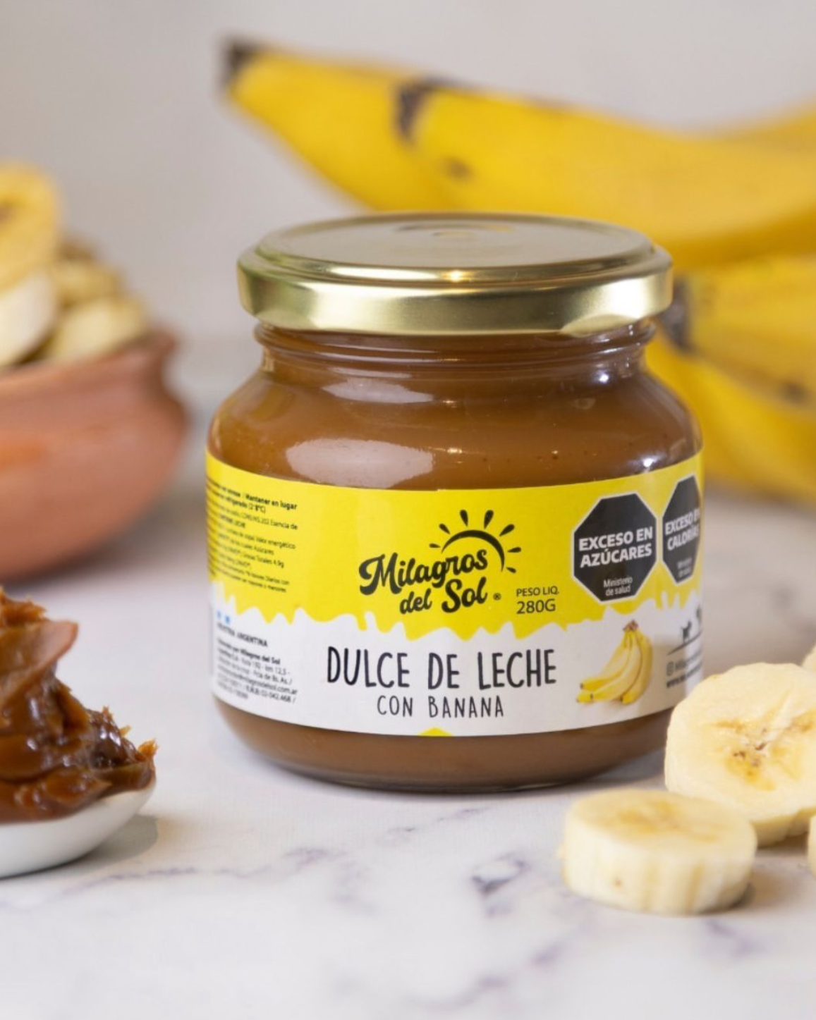 Tarro de dulce de leche con sabor a banana, etiqueta amarilla, bananas al fondo, rodajas en primer plano.