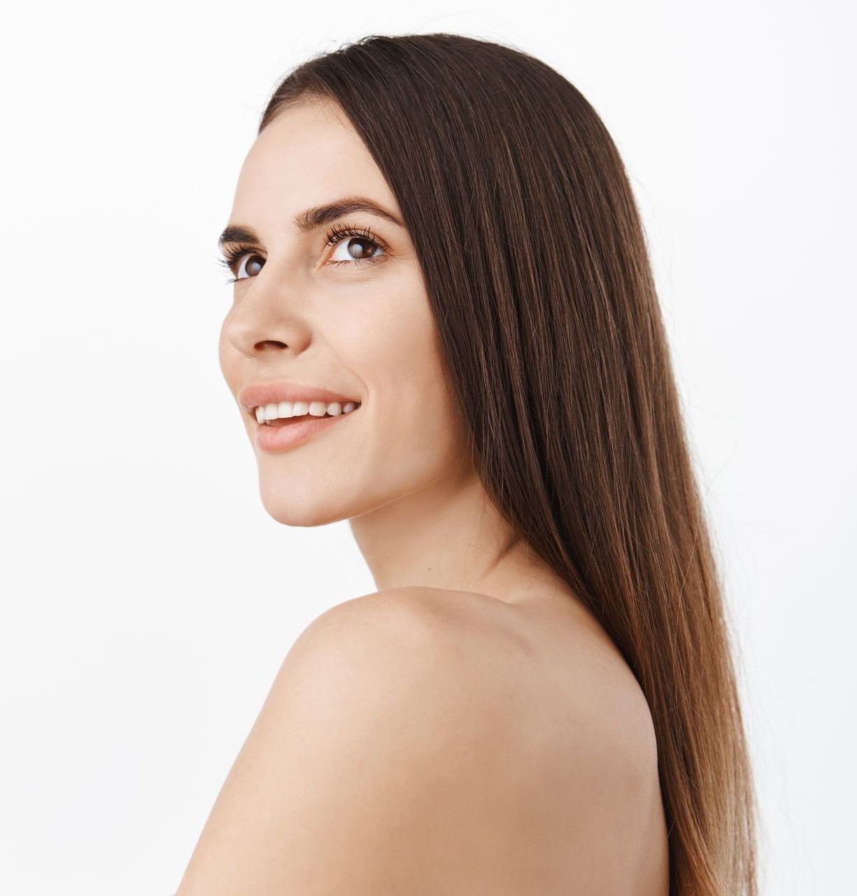 A woman with long hair is smiling and looking over her shoulder.