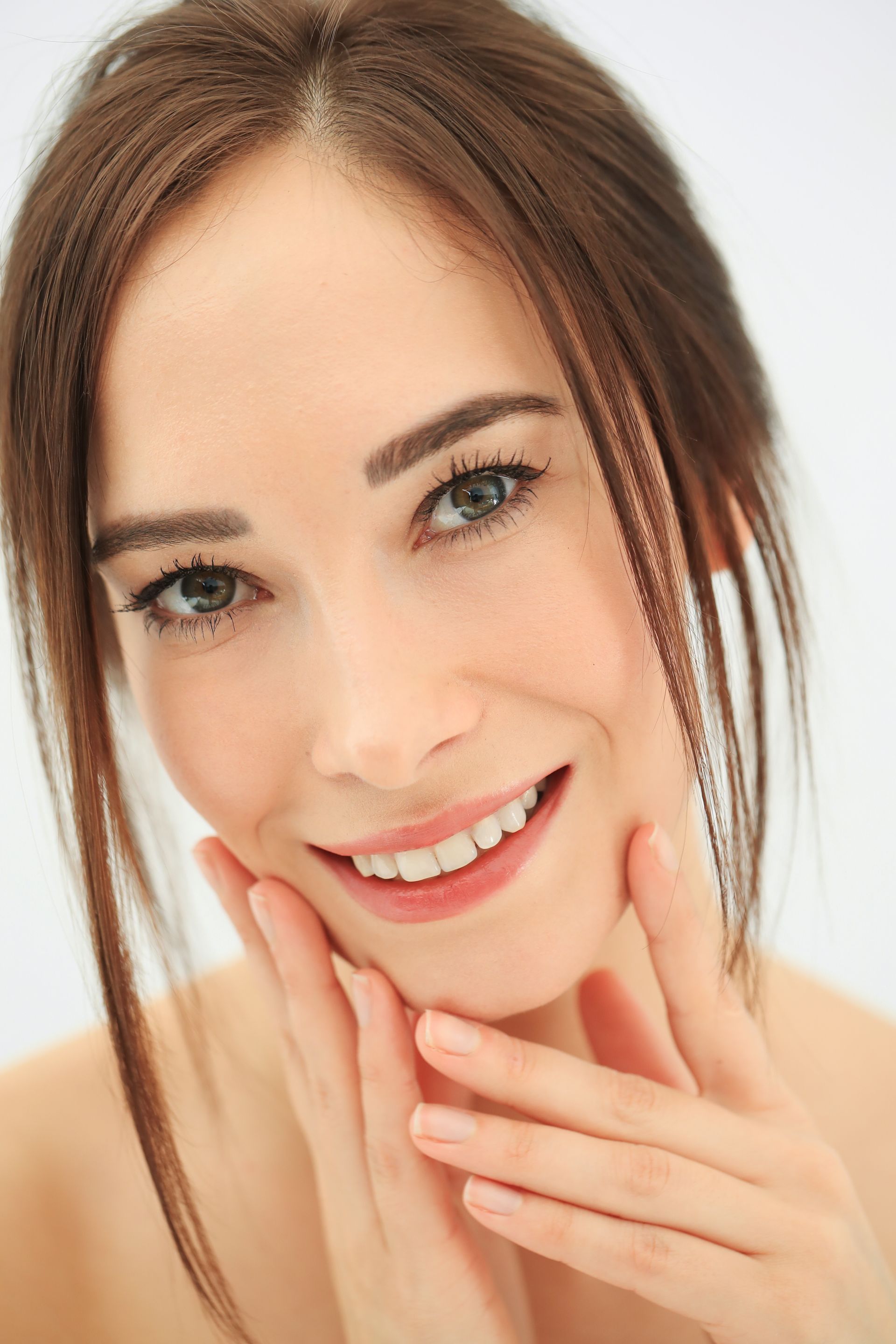 A woman is smiling and touching her face with her hands.