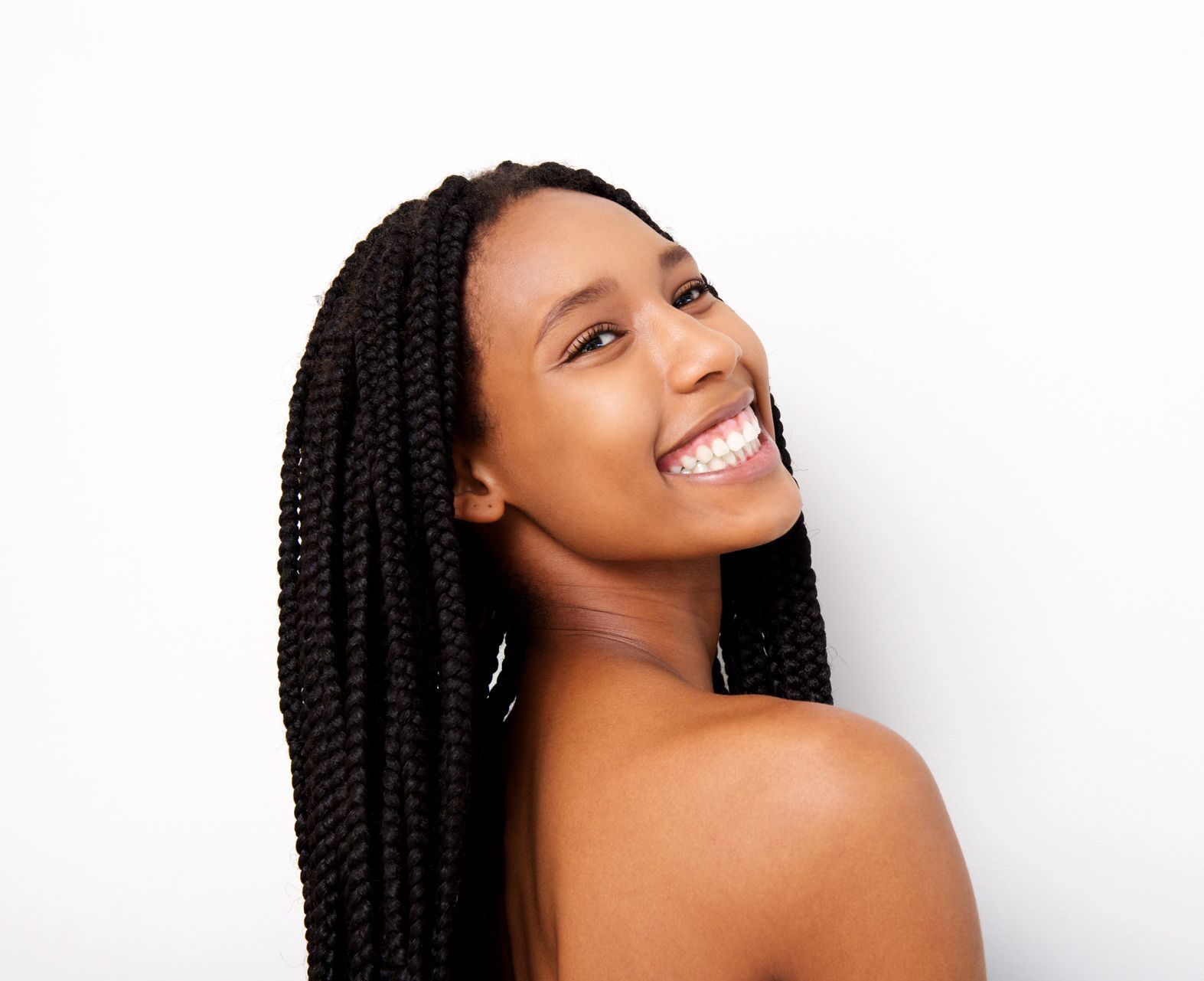 A woman with braids is smiling and looking over her shoulder.