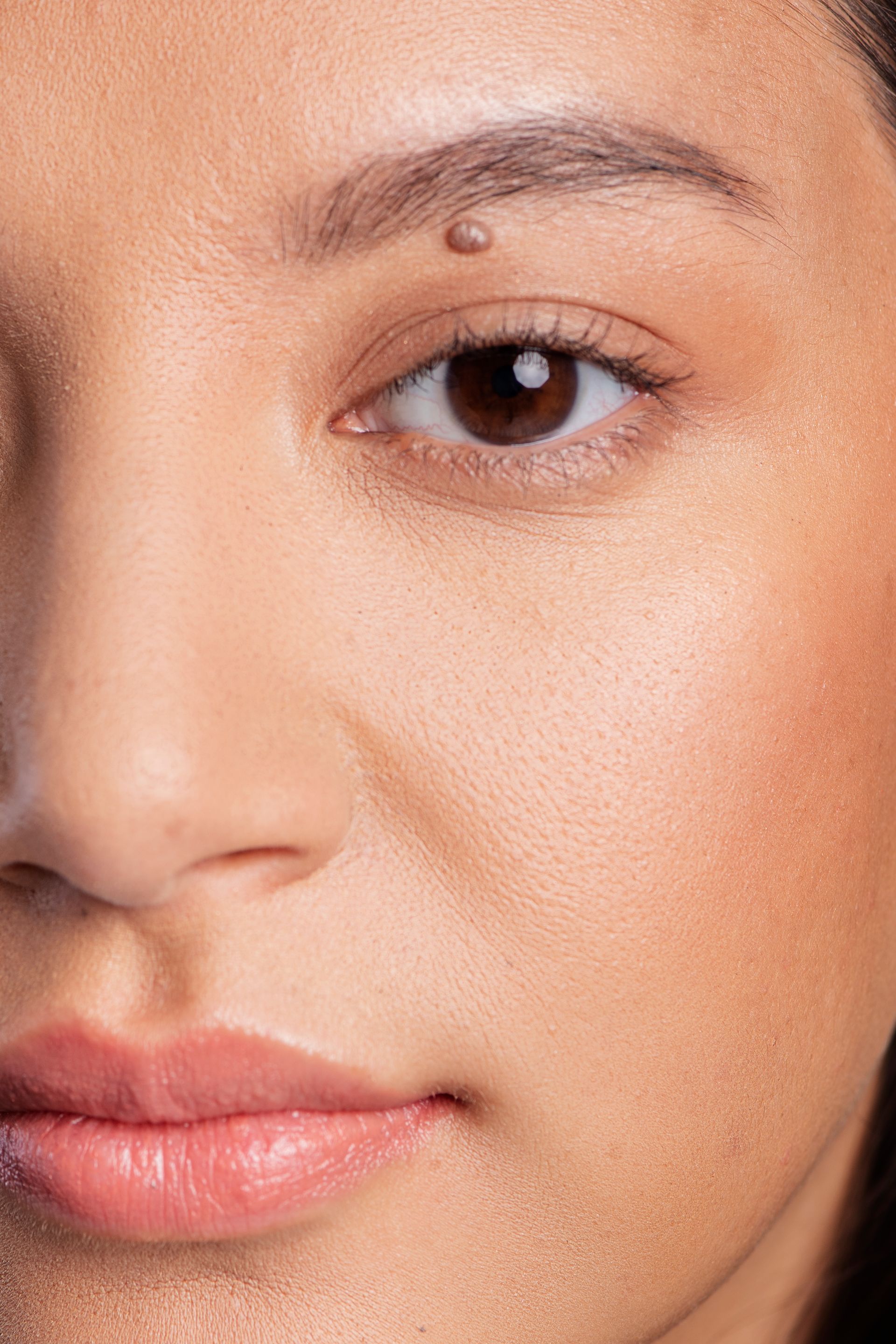 A close up of a woman 's face with a mole on her eyebrow.