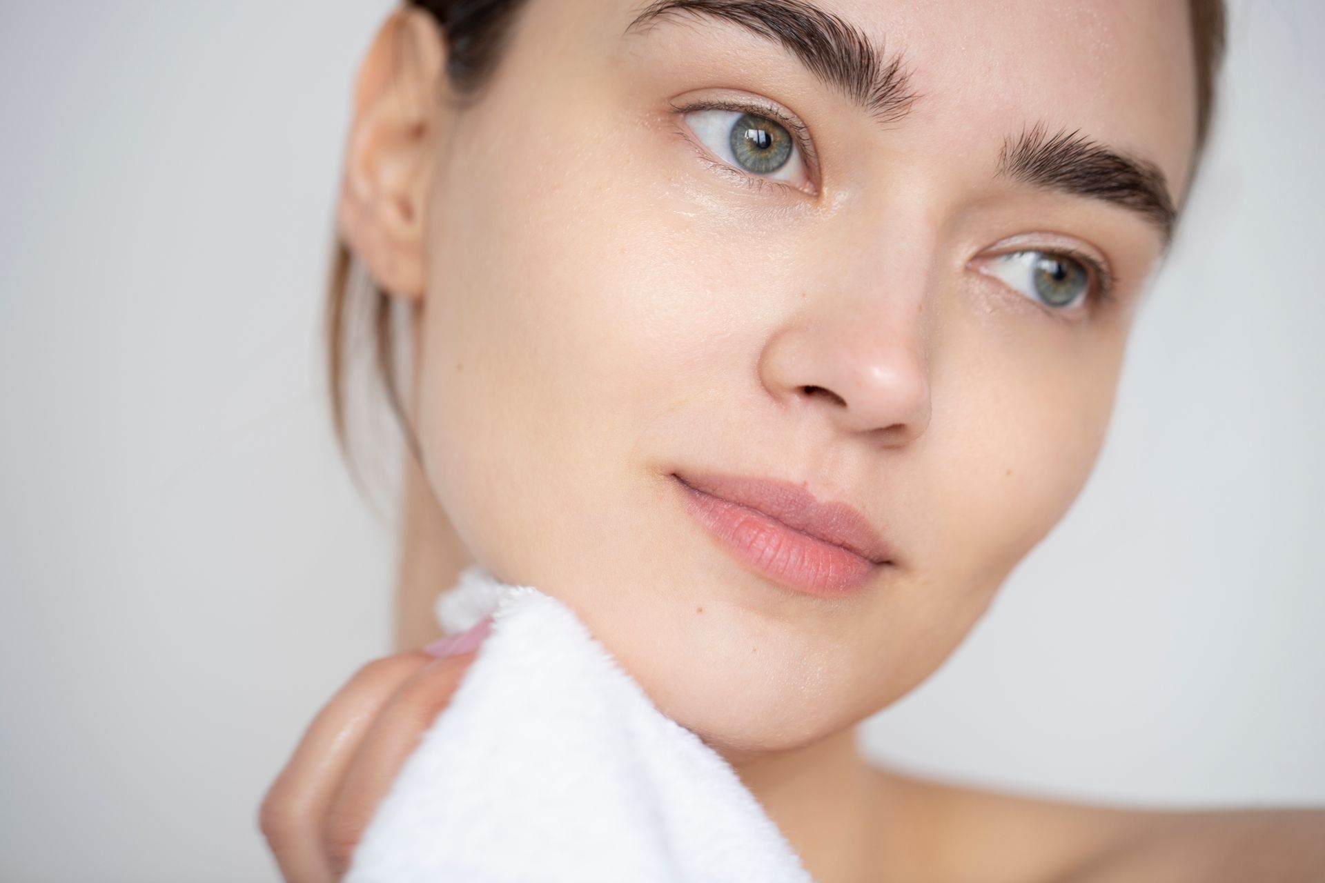 A woman is cleaning her face with a towel.