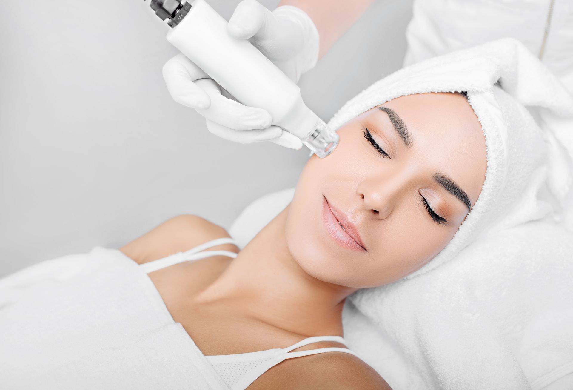 A woman with a towel wrapped around her head is getting a facial treatment.