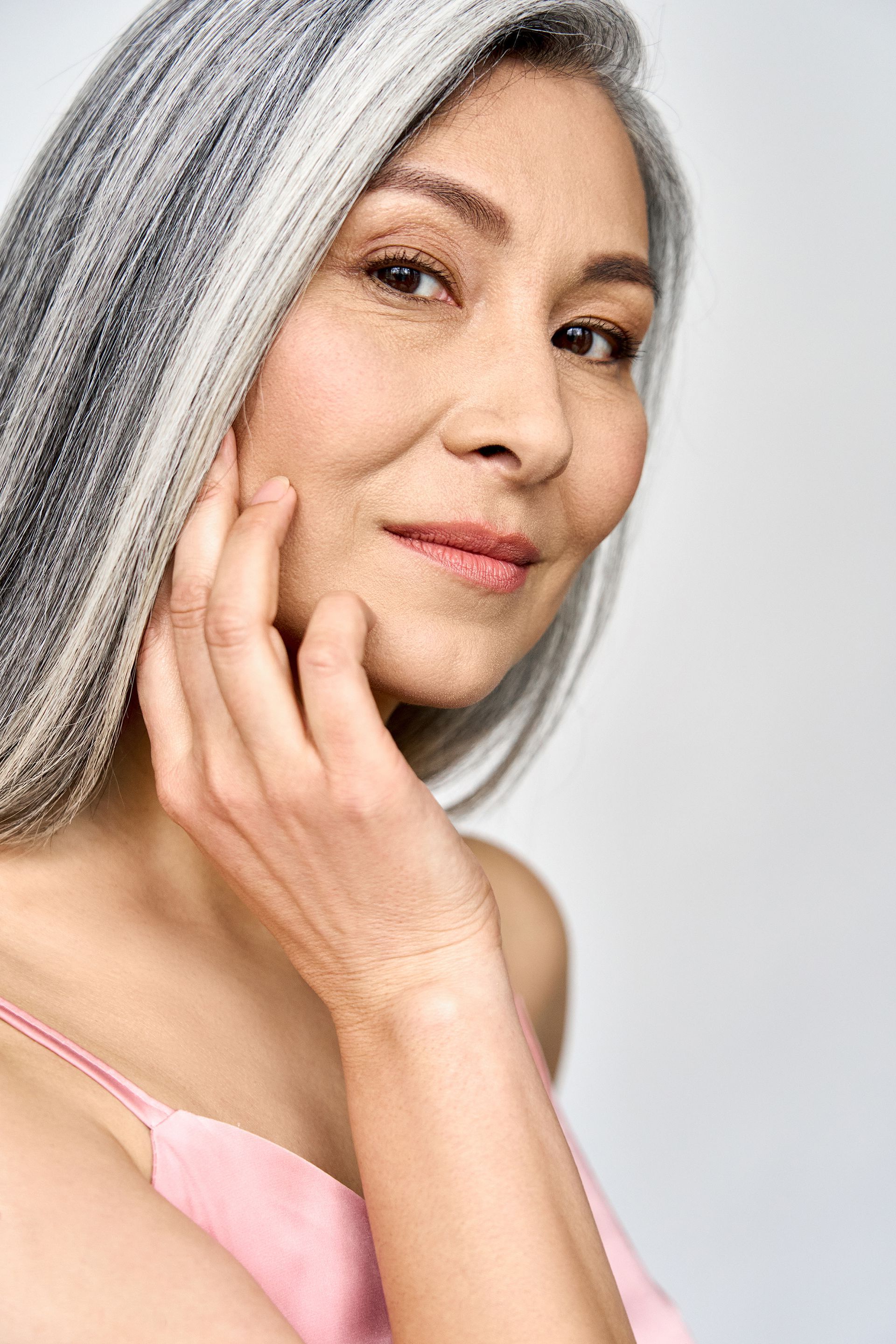A woman with gray hair is touching her face and smiling.