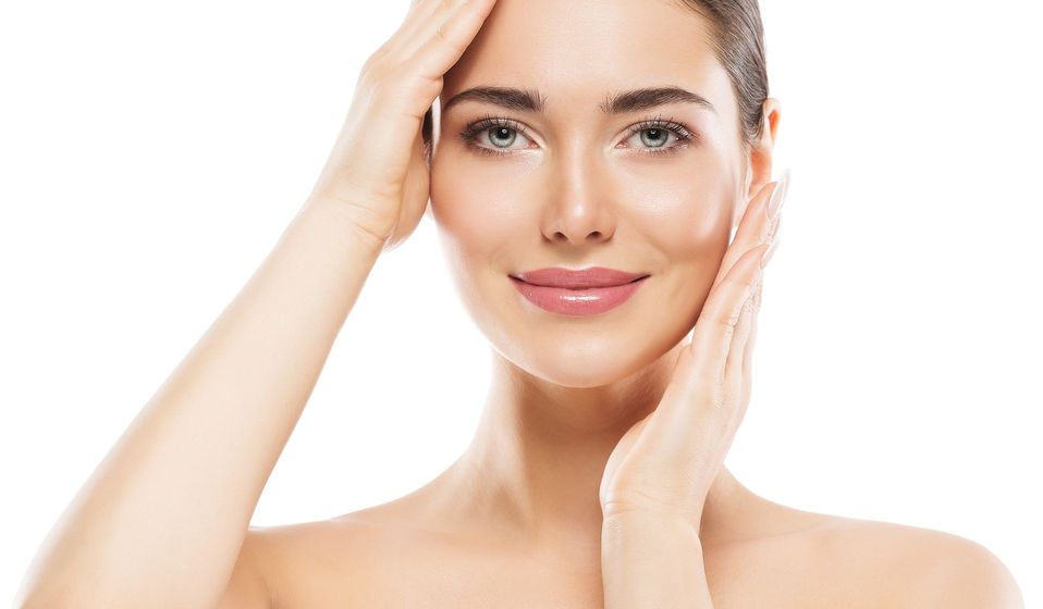 A woman is touching her face with her hands and smiling.