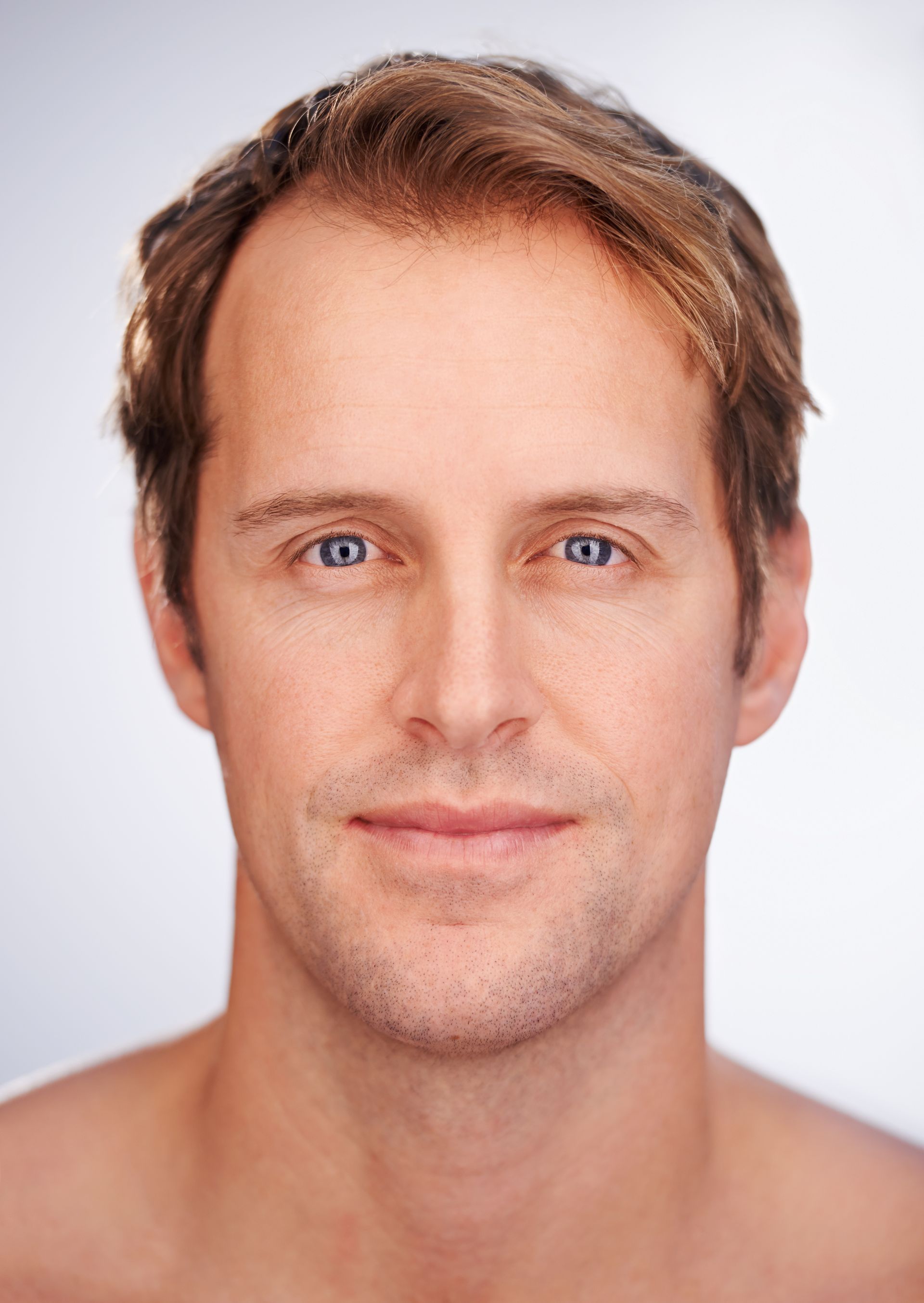 A man without a shirt is smiling for the camera.