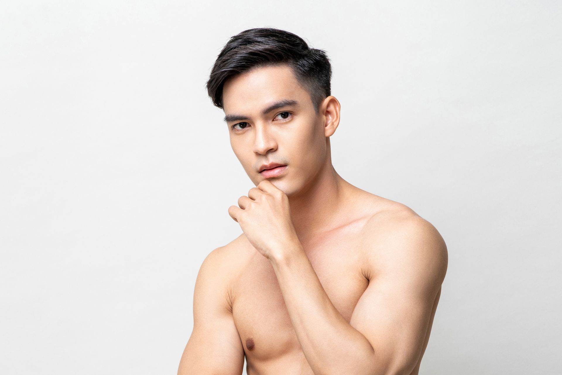A shirtless man with his hand on his chin is looking at the camera.