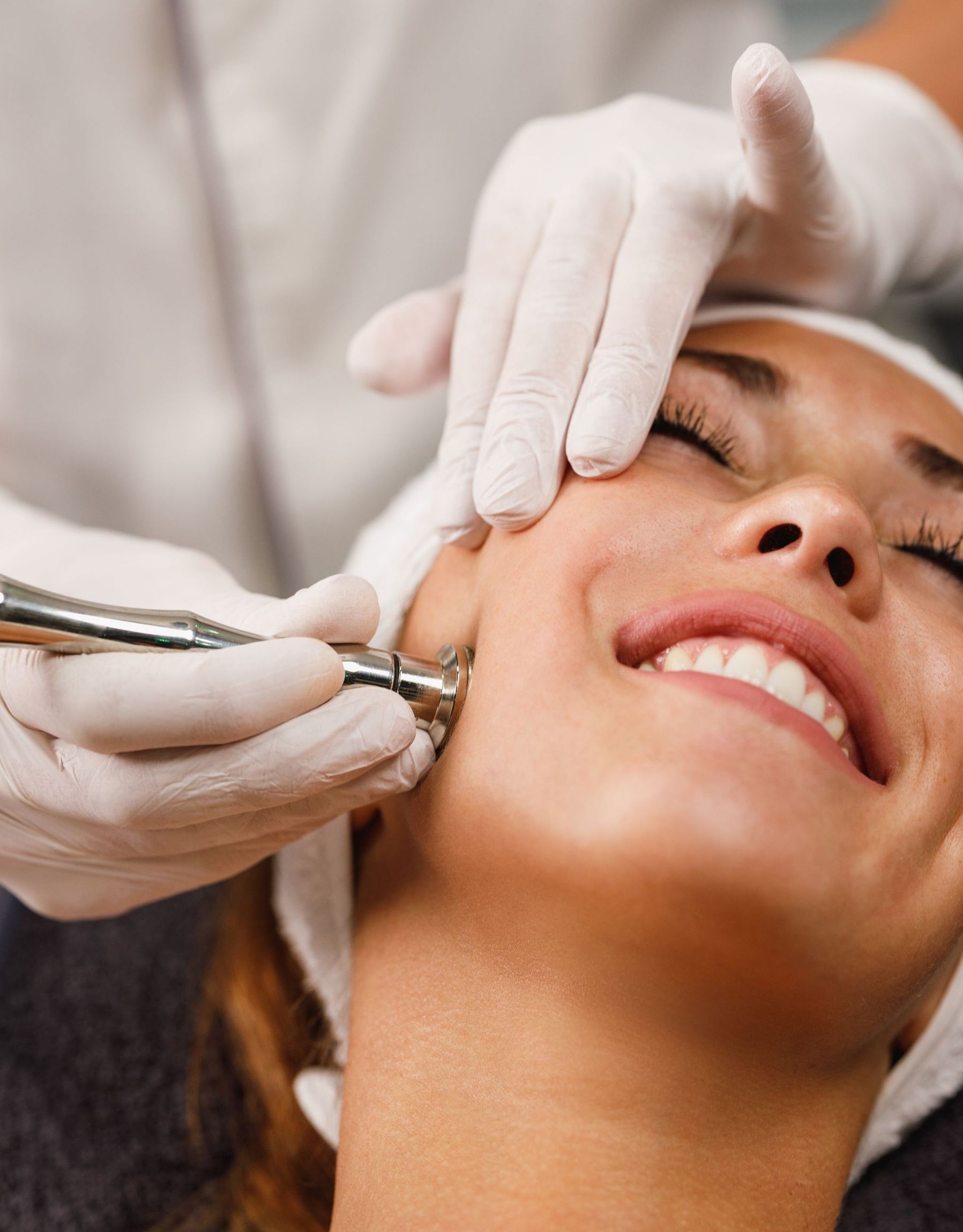 A woman is smiling while getting a facial treatment