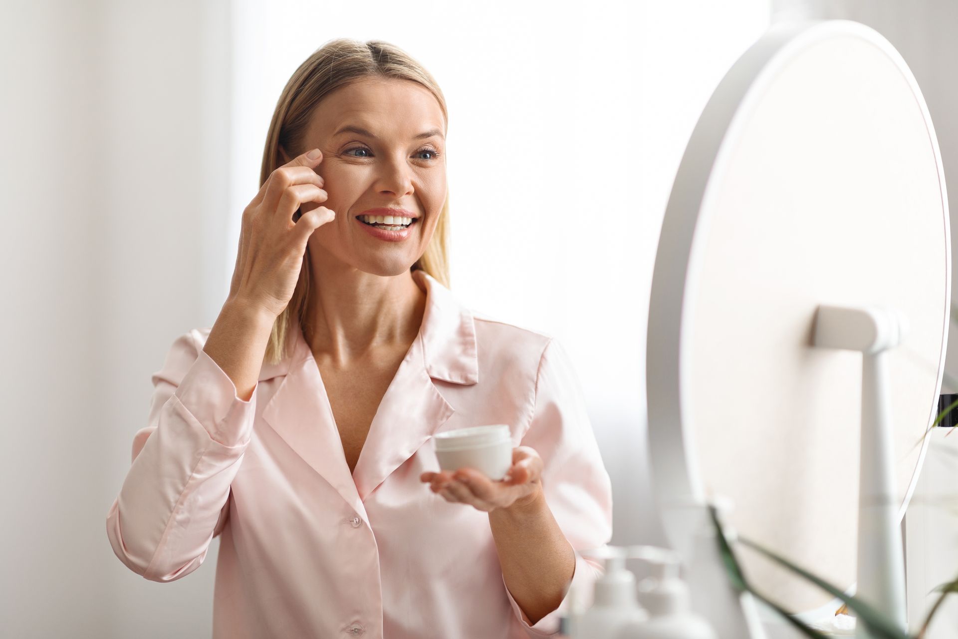 A woman is applying a cream to her face in front of a mirror.