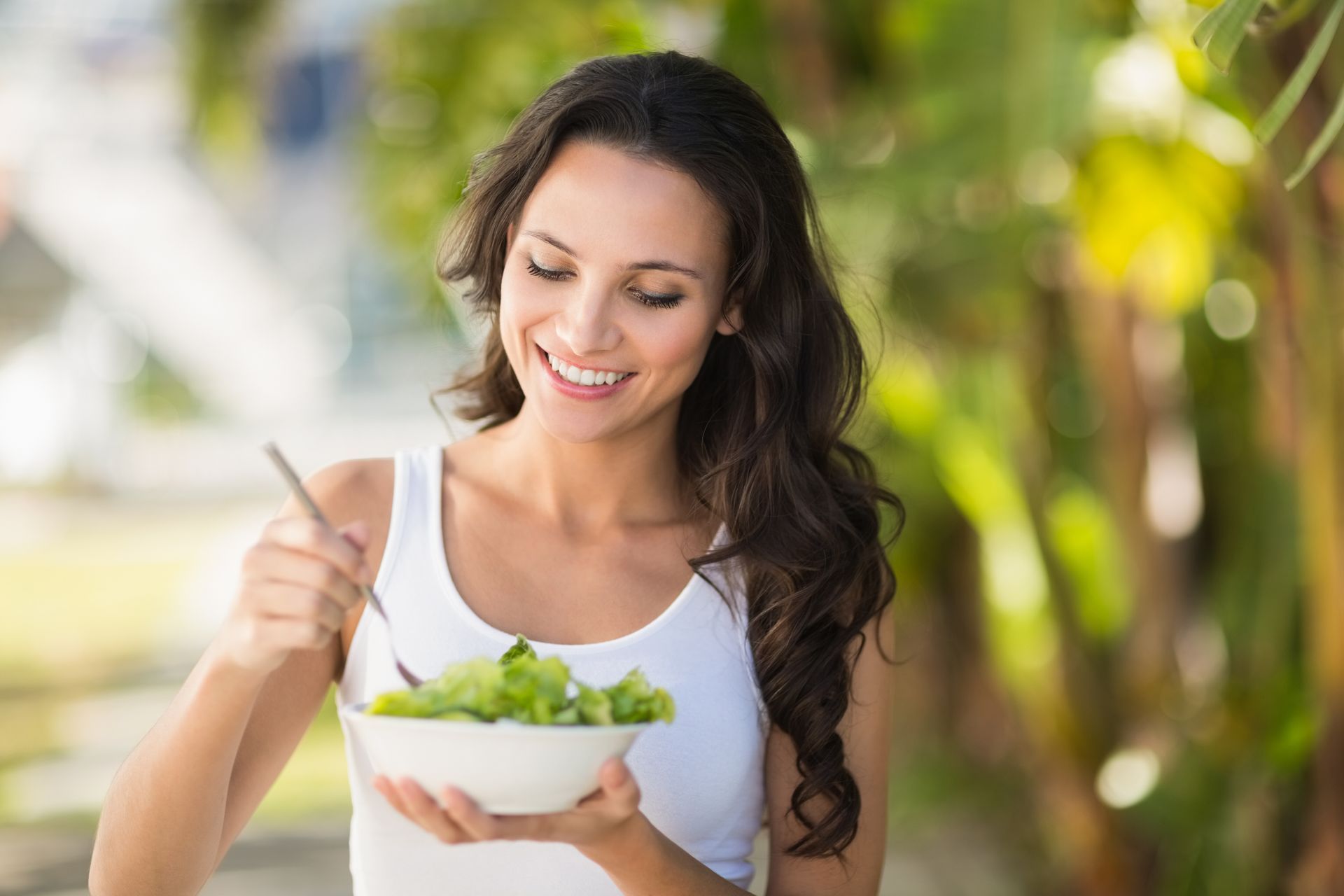 A woman is eating a salad from a bowl with a fork.