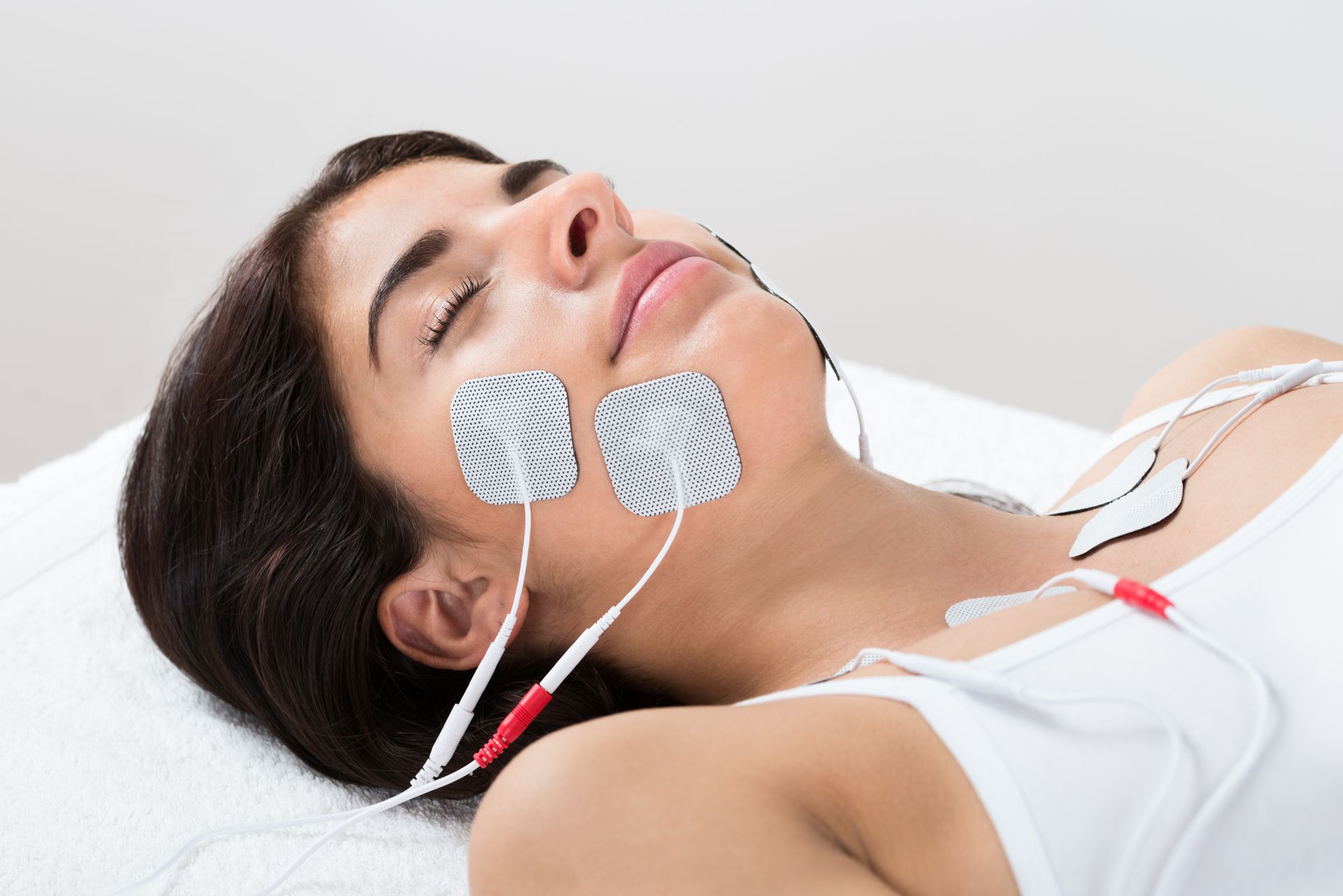 A woman is laying on a bed with electrodes attached to her face.
