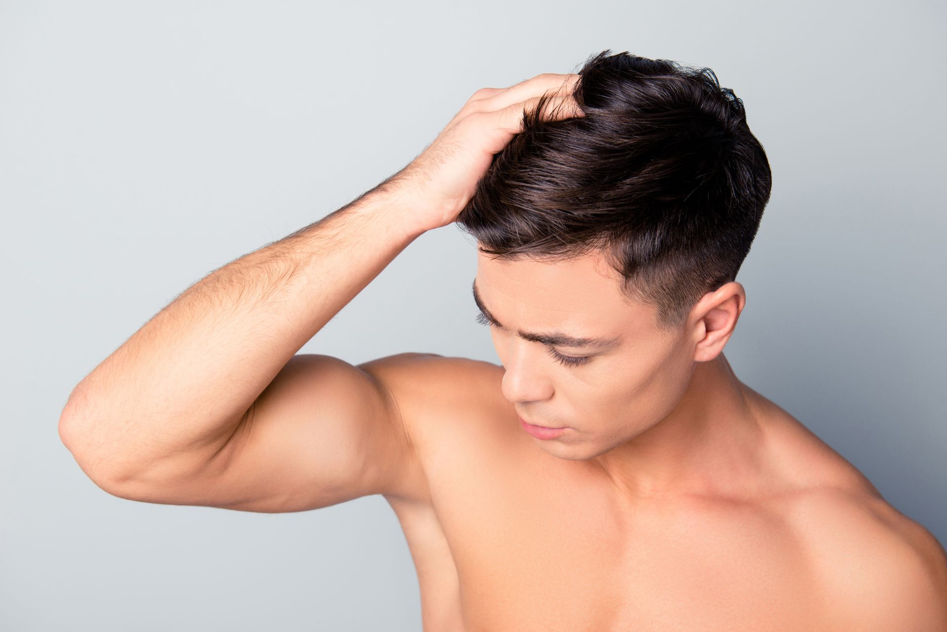 A shirtless man is scratching his head with his hand.