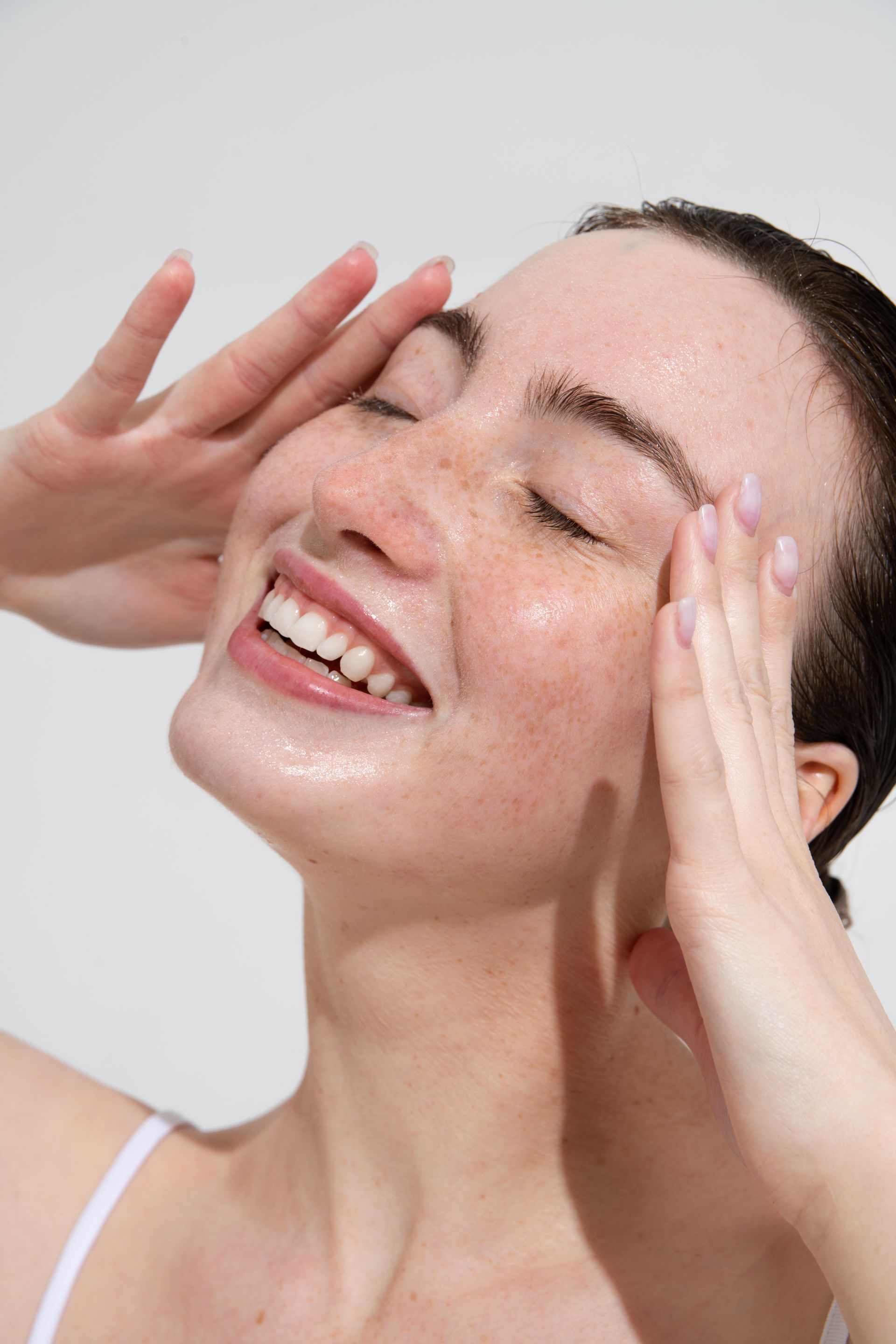 A woman is smiling while cleaning her face with her hands.