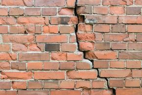 Mur de briques fissuré avec une grande fissure verticale; briques orange et brunes.