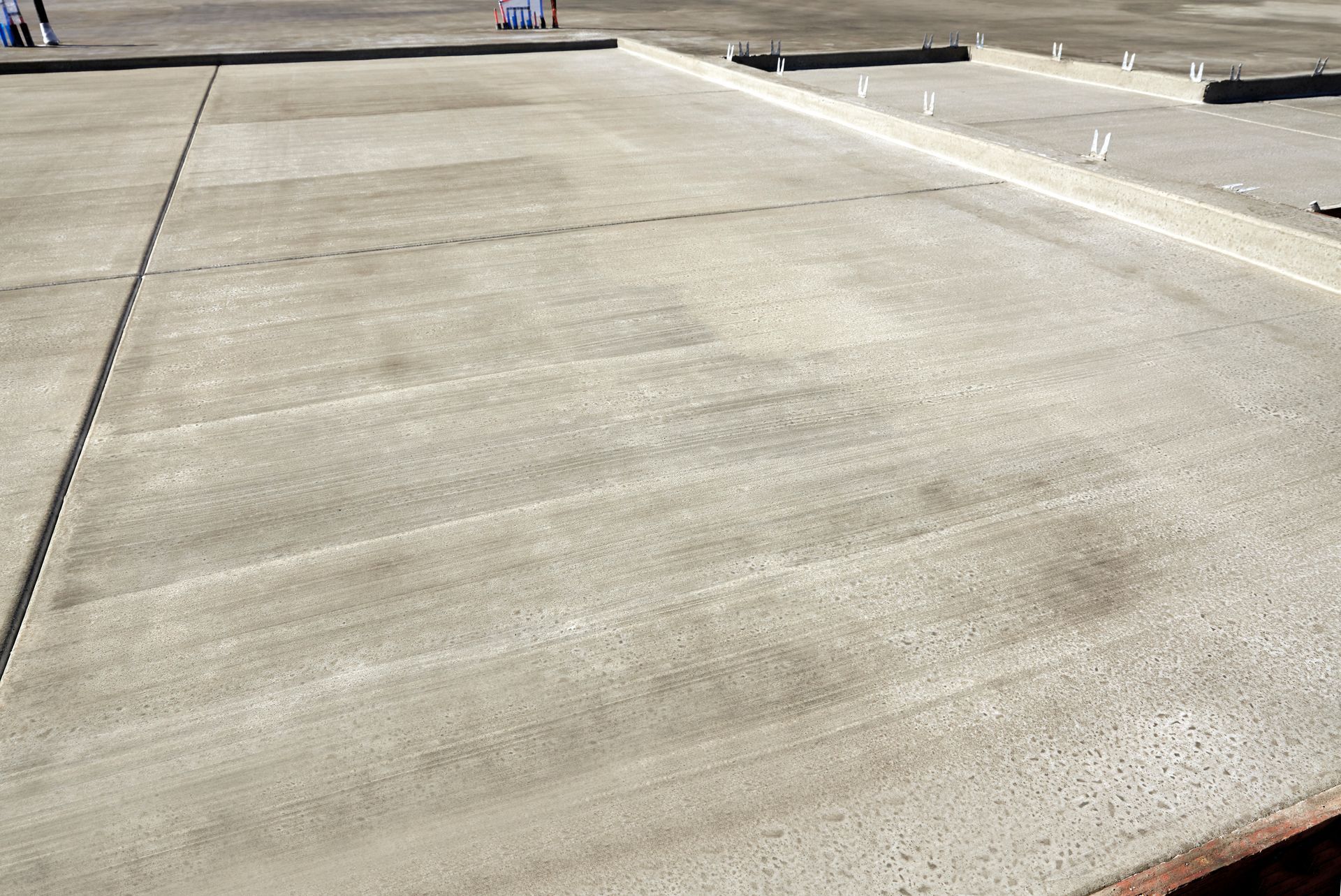 Surface de béton fraîchement coulée, avec des traces de truelle visibles et un décor de chantier.