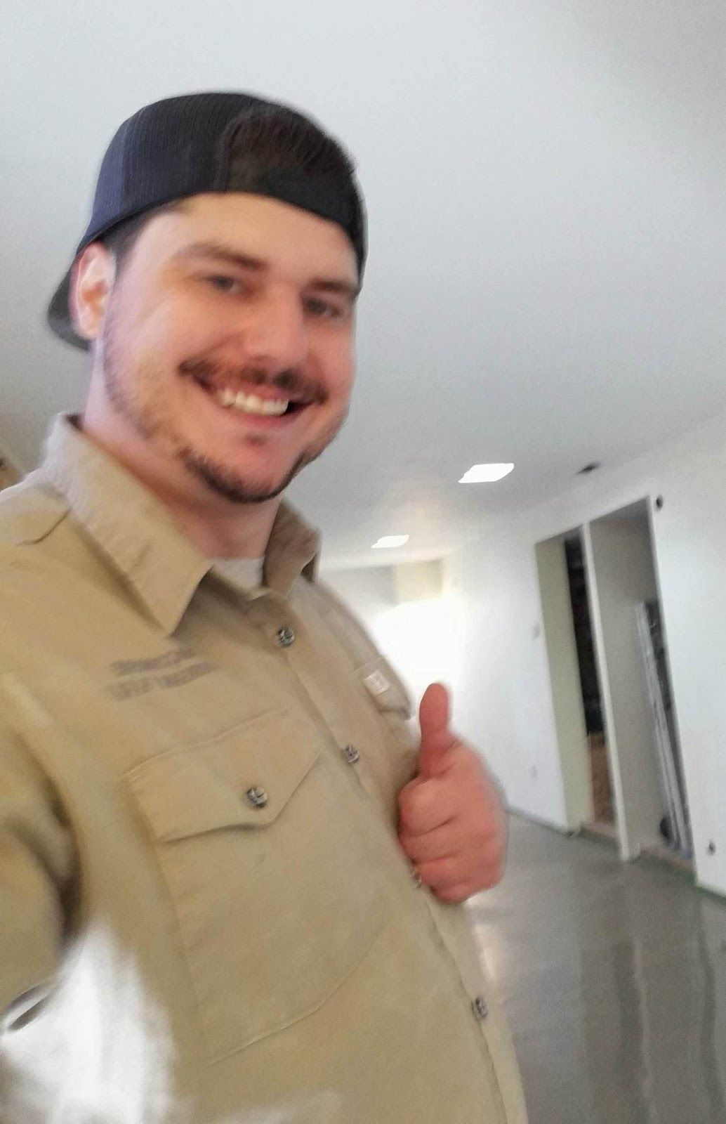 Homme en uniforme de travail avec les pouces levés, souriant, dans une pièce en construction.