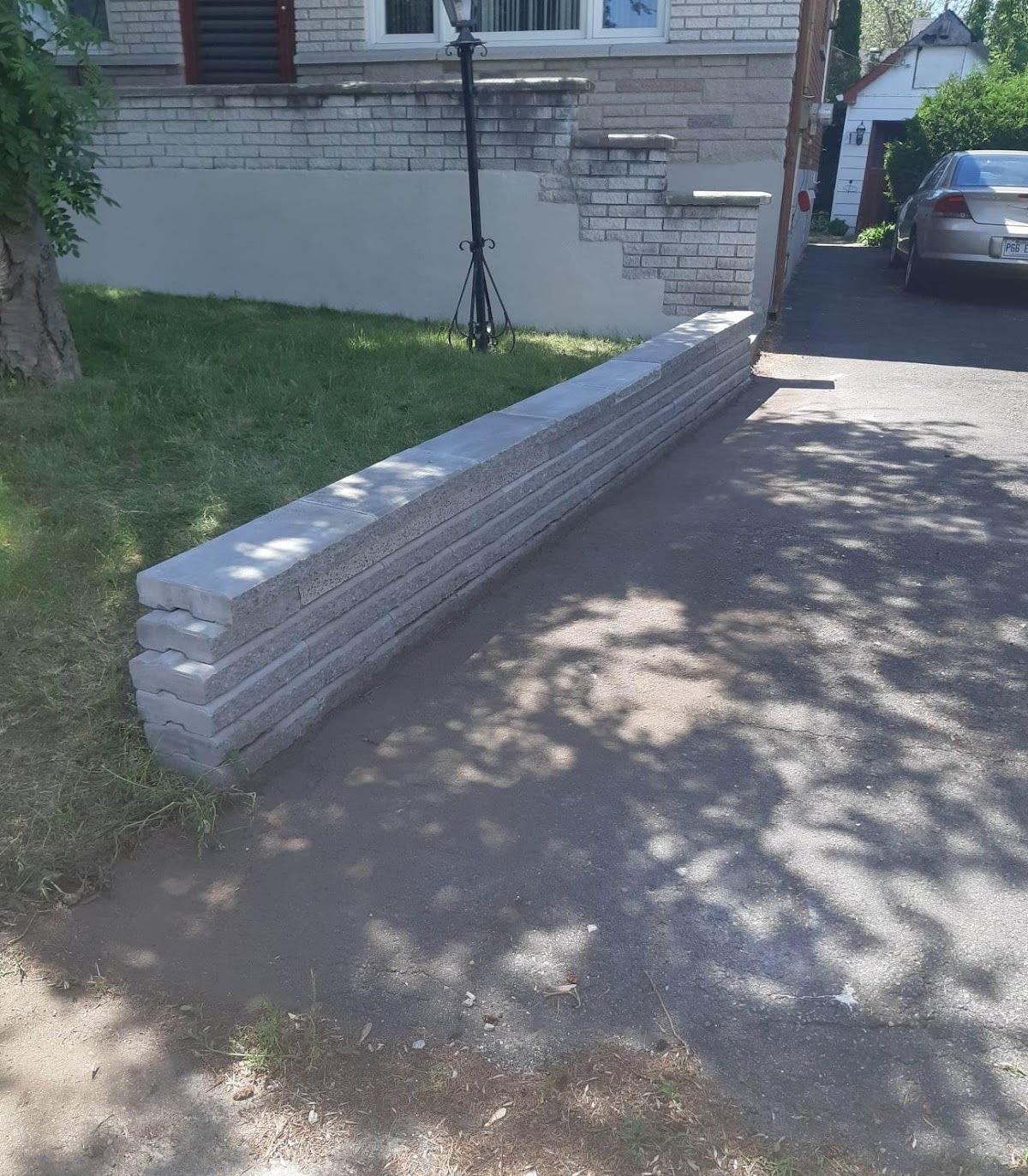 Une pile de blocs de béton gris se trouve sur une allée près d'une maison et d'une cour herbeuse.