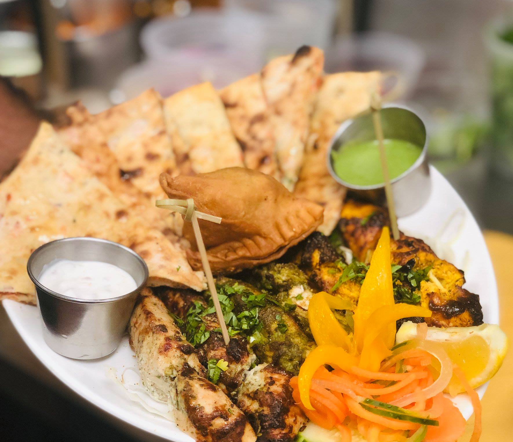 Plate of Indian appetizers, including naan, samosa, and grilled meats, with dipping sauces.