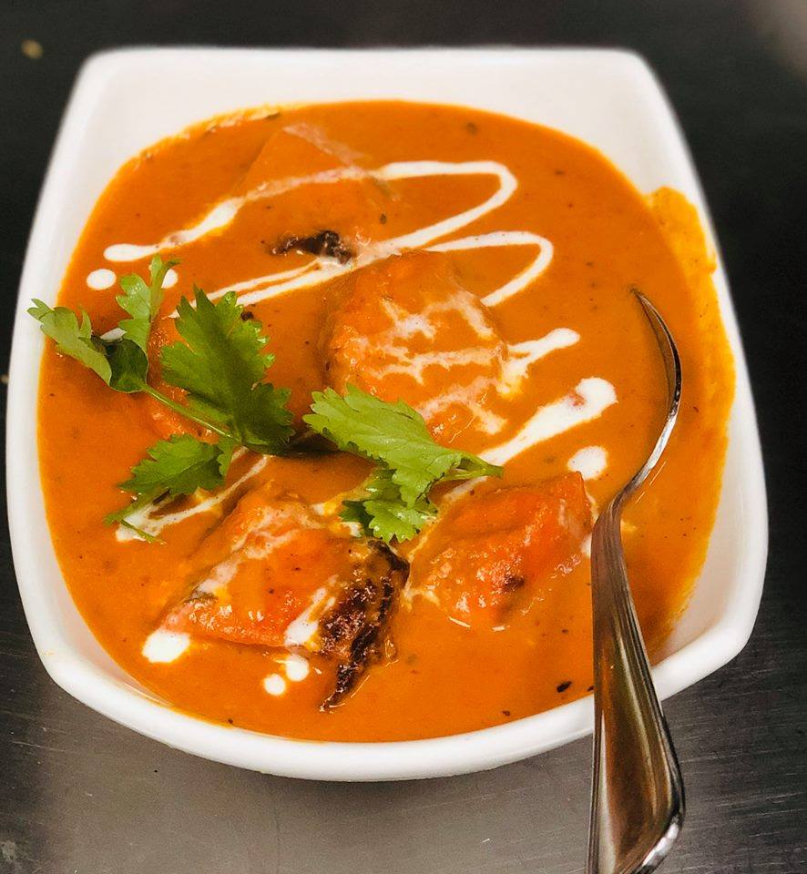 Butter chicken dish in a white bowl, garnished with cilantro and cream swirls, with a silver spoon.
