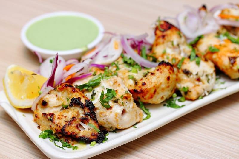 Grilled chicken pieces with salad, herbs, lemon, and green sauce on a white plate.