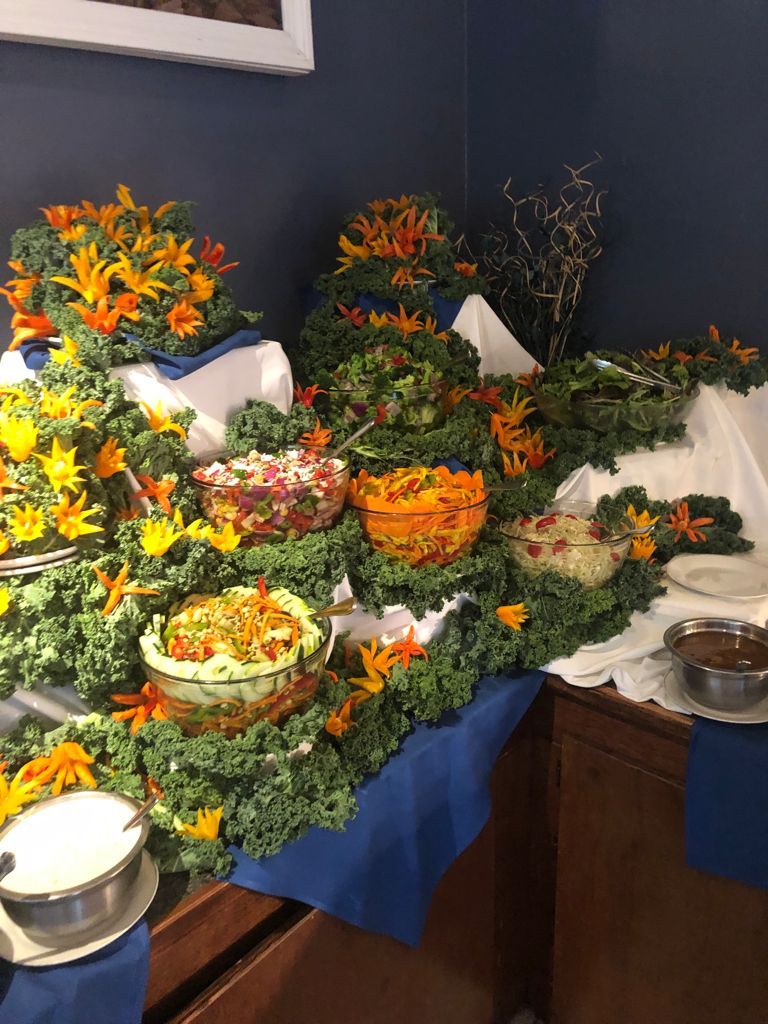 Buffet table with various salads in glass bowls, decorated with kale and orange flowers.