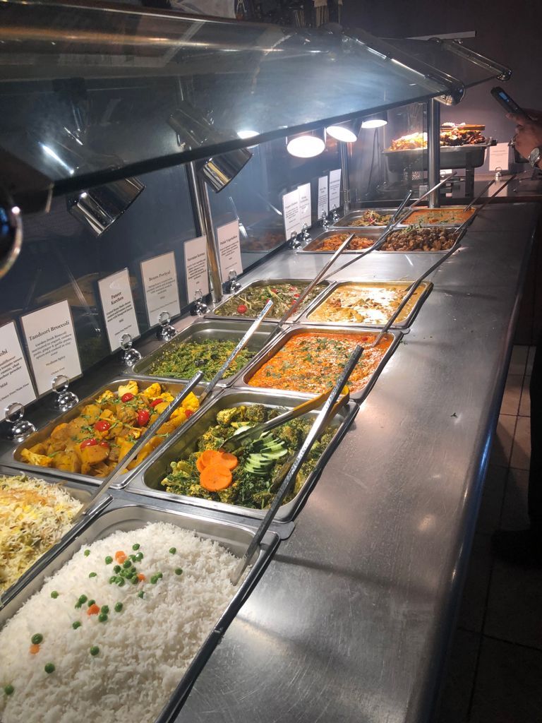 Buffet with various food dishes in stainless steel serving trays under bright lights.