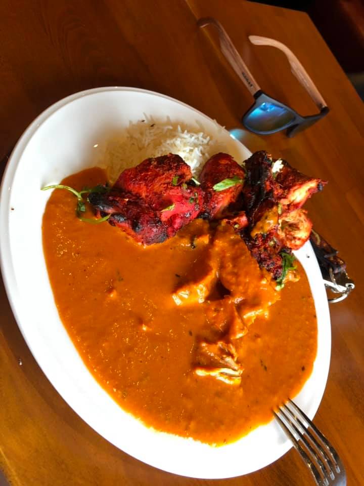 Plate of Indian food: Tandoori chicken, butter chicken, rice, on a white plate.