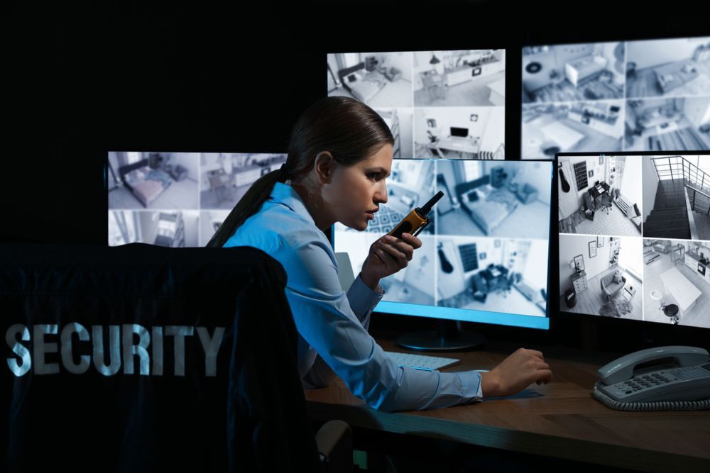 A Woman in Security Room, Monitoring Multiple Screens, Holding Radio, at a Desk — Clinton Security Services In Moree, NSW