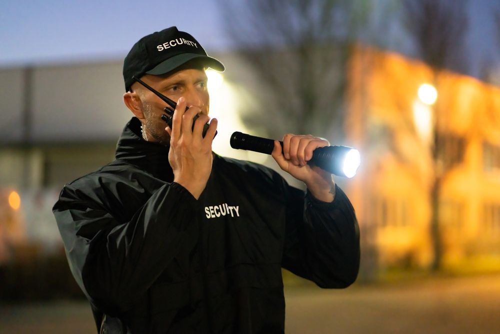 A Security Guard Talking Into a Walkie-talkie, Holding a Flashlight, at Night — Clinton Security Services In Brisbane, QLD