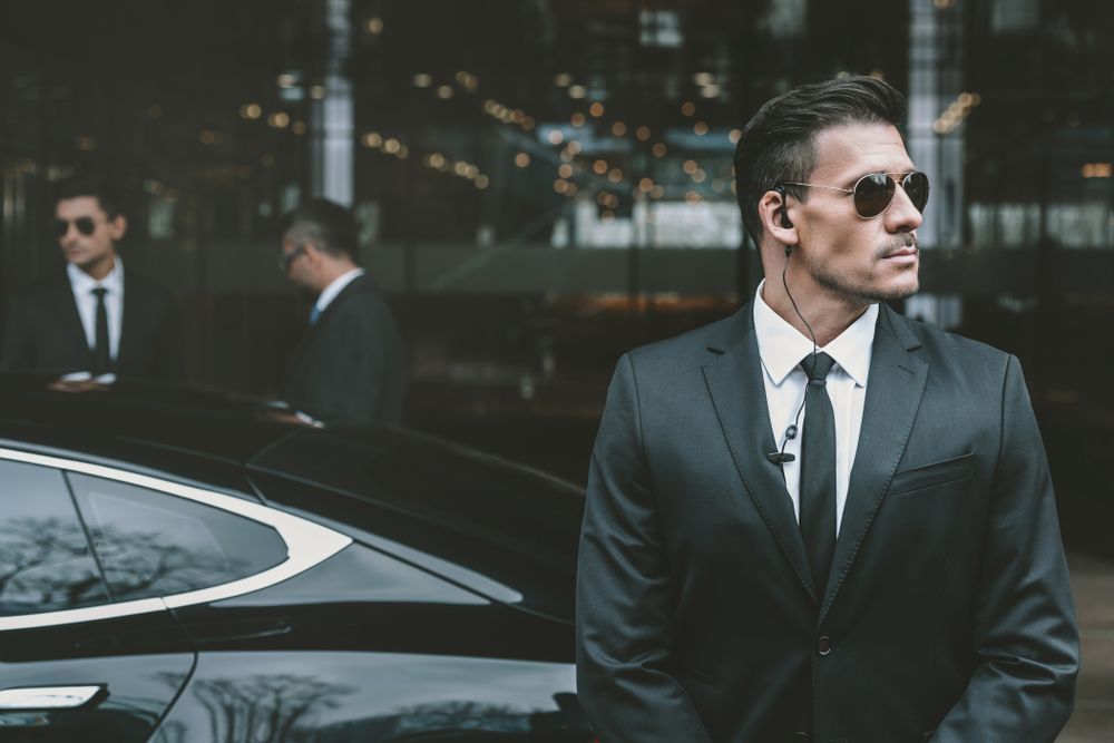 Bodyguards in Suits and Sunglasses Standing Near a Black Car — Clinton Security Services In Armidale, NSW
