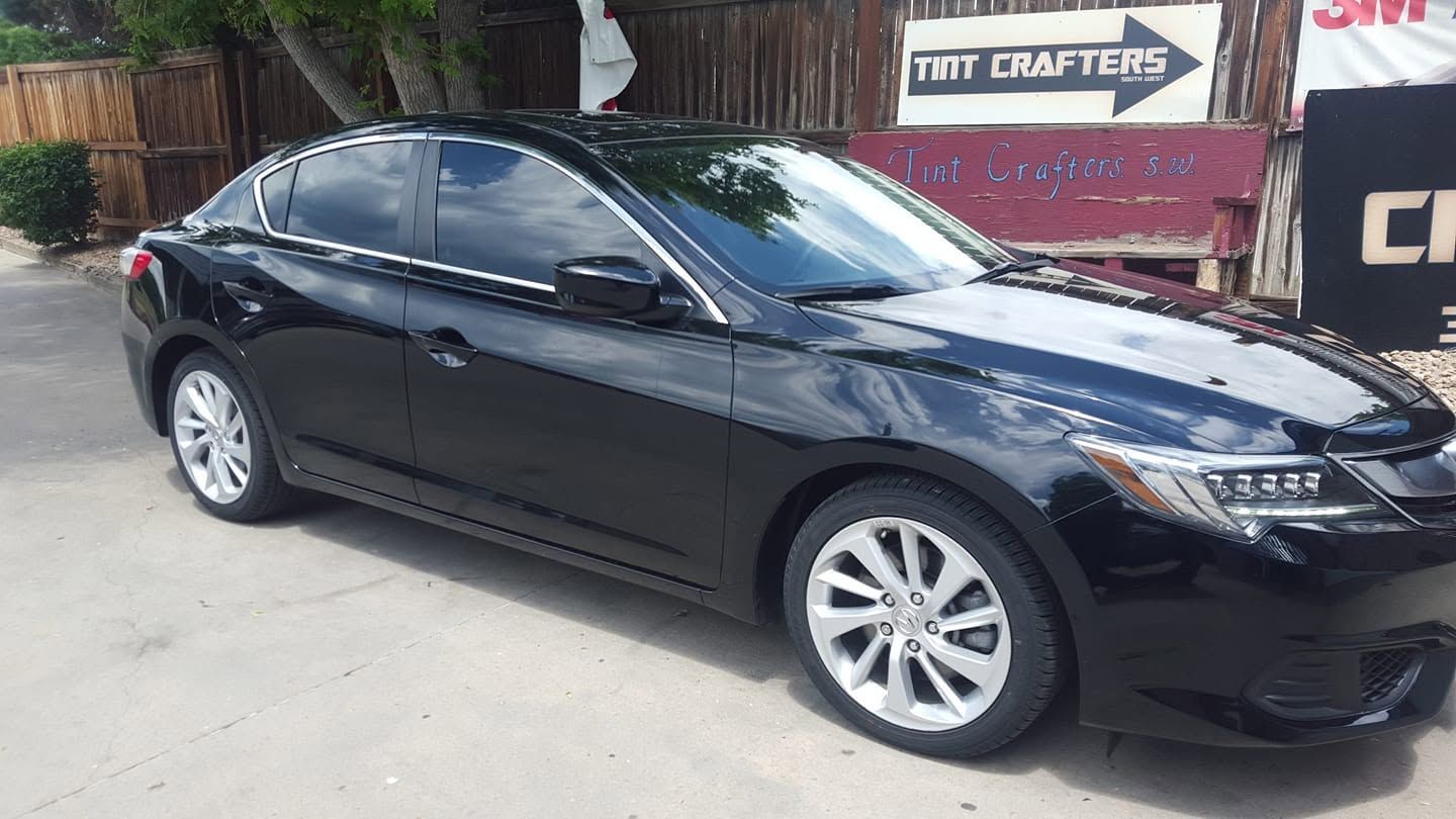 Black sedan parked outdoors near a storefront, side view.