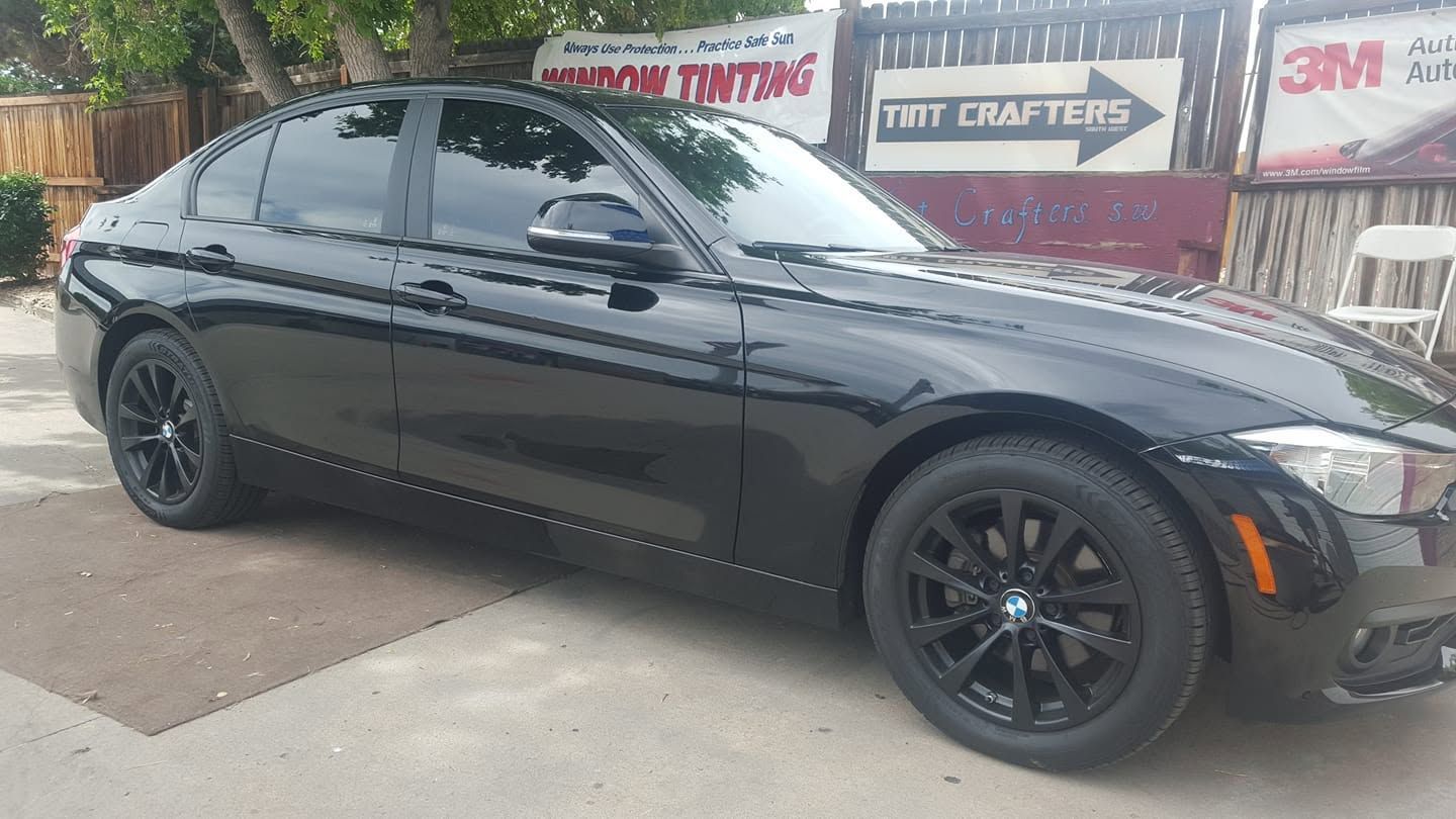 Black sedan parked outdoors beside a shop sign, with dark tinted windows and black wheels.