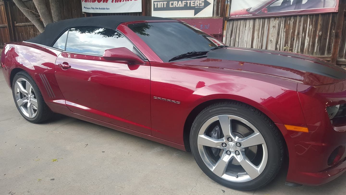 Red convertible sports car parked beside a wooden fence on a paved street.