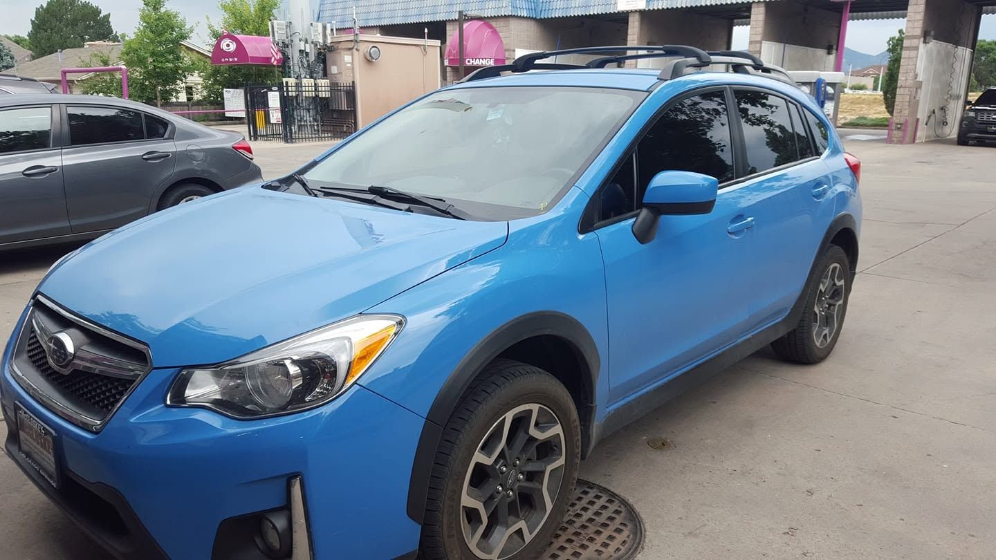 Blue SUV parked on a city street near buildings and a manhole cover