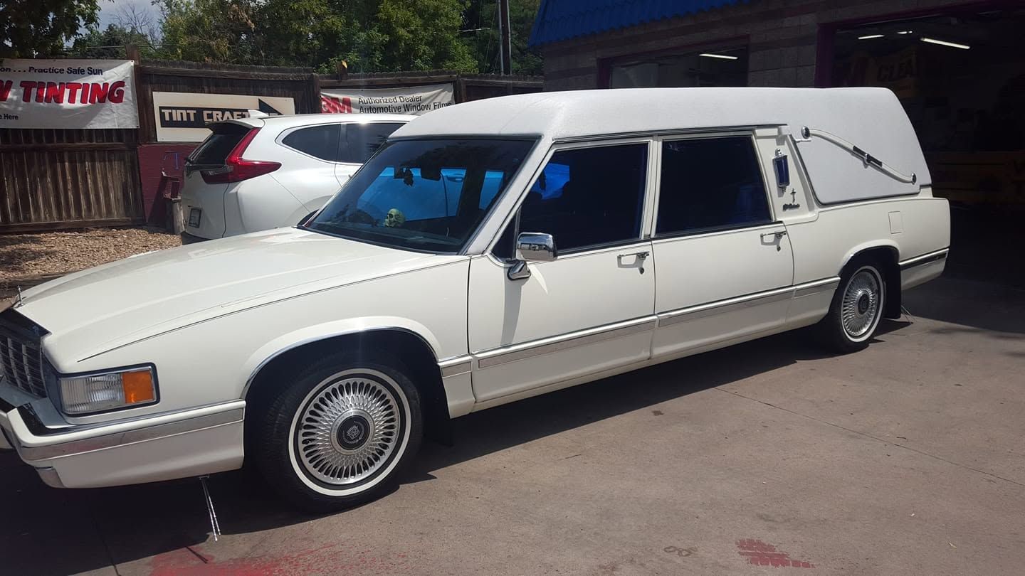 White hearse parked outdoors in a lot, shown in side view with rear windows covered.