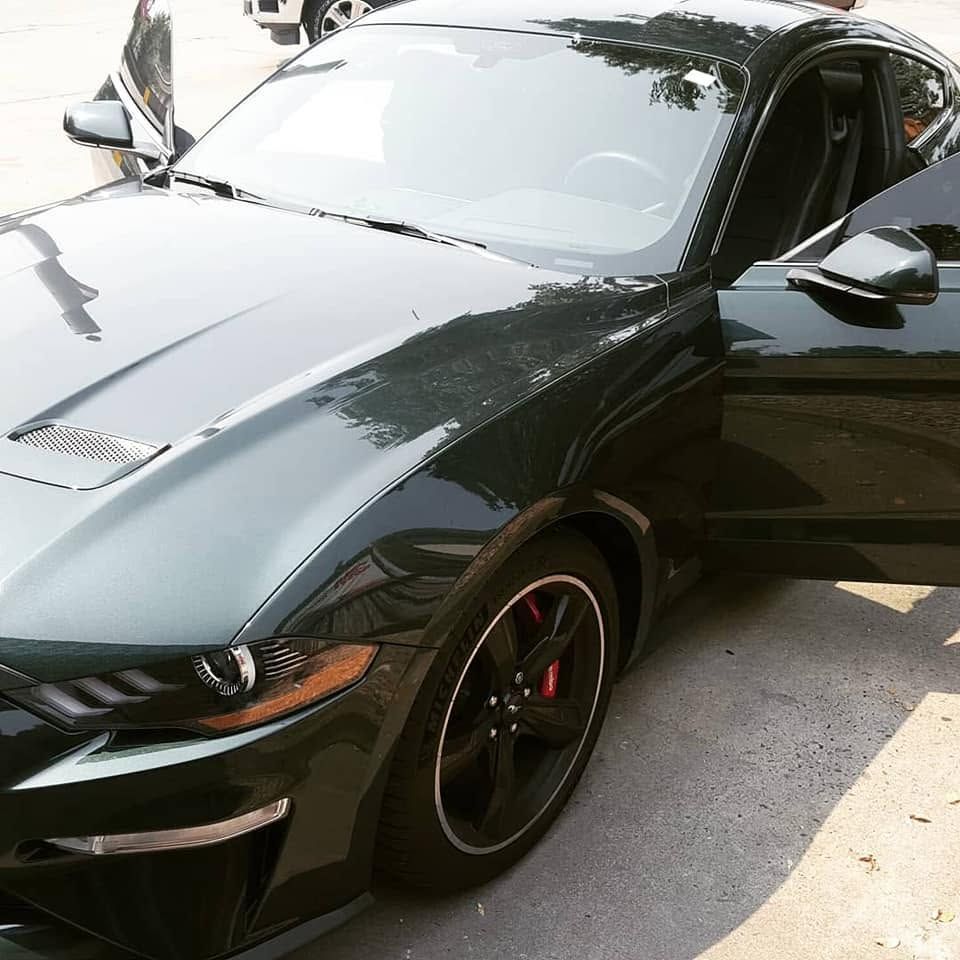 Black sports coupe with glossy finish parked outdoors, driver’s door open and headlights visible