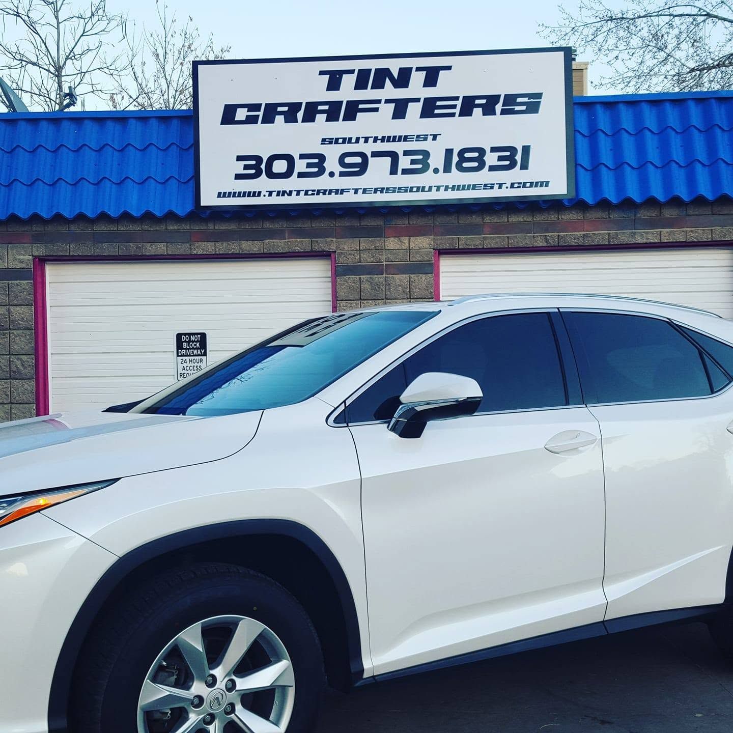 White SUV parked outside Tint Crafters shop with blue roof and sign in front.