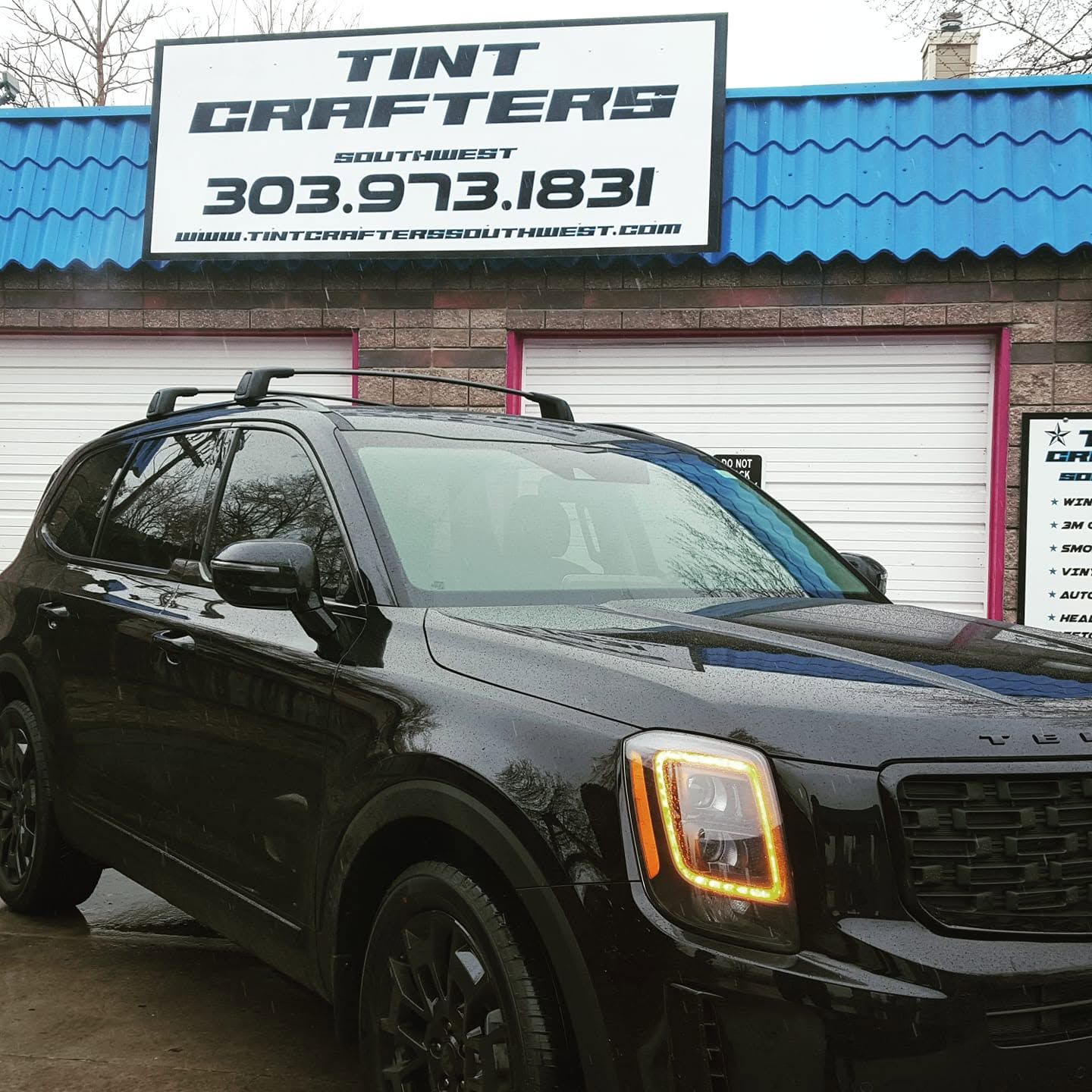 Black SUV parked outside Tint Crafters storefront with blue roof and sign above it