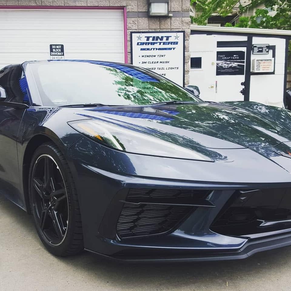 Black sports car parked outside a tint shop with a garage door and sign in the background